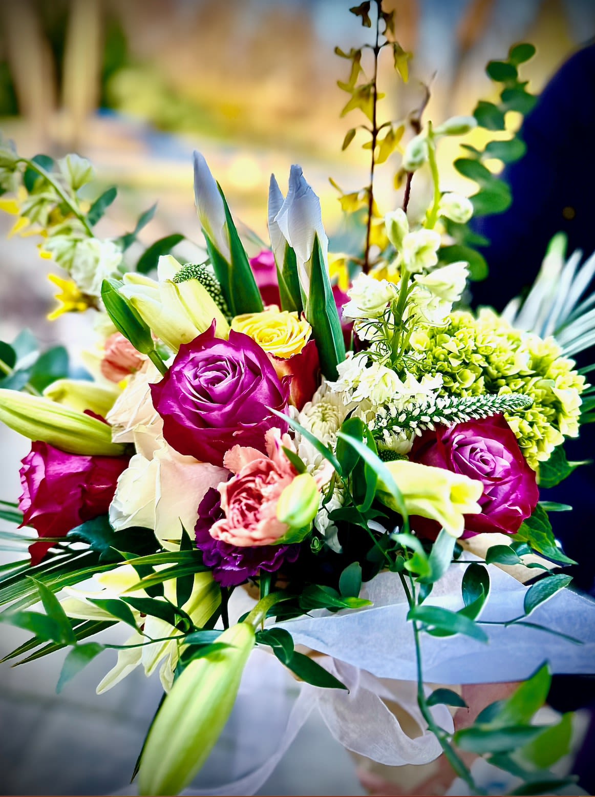 Farm and Fancy Bouquet - Our Farm and Fancy vibrant bouquet features a delightful mix of locally sourced, seasonal blooms paired with timeless roses and lush greens. Expertly hand-tied and wrapped, this arrangement brings a touch of elegance and fresh charm to any occasion.  If you would like this arranged in a vase, please updgrade to premium.