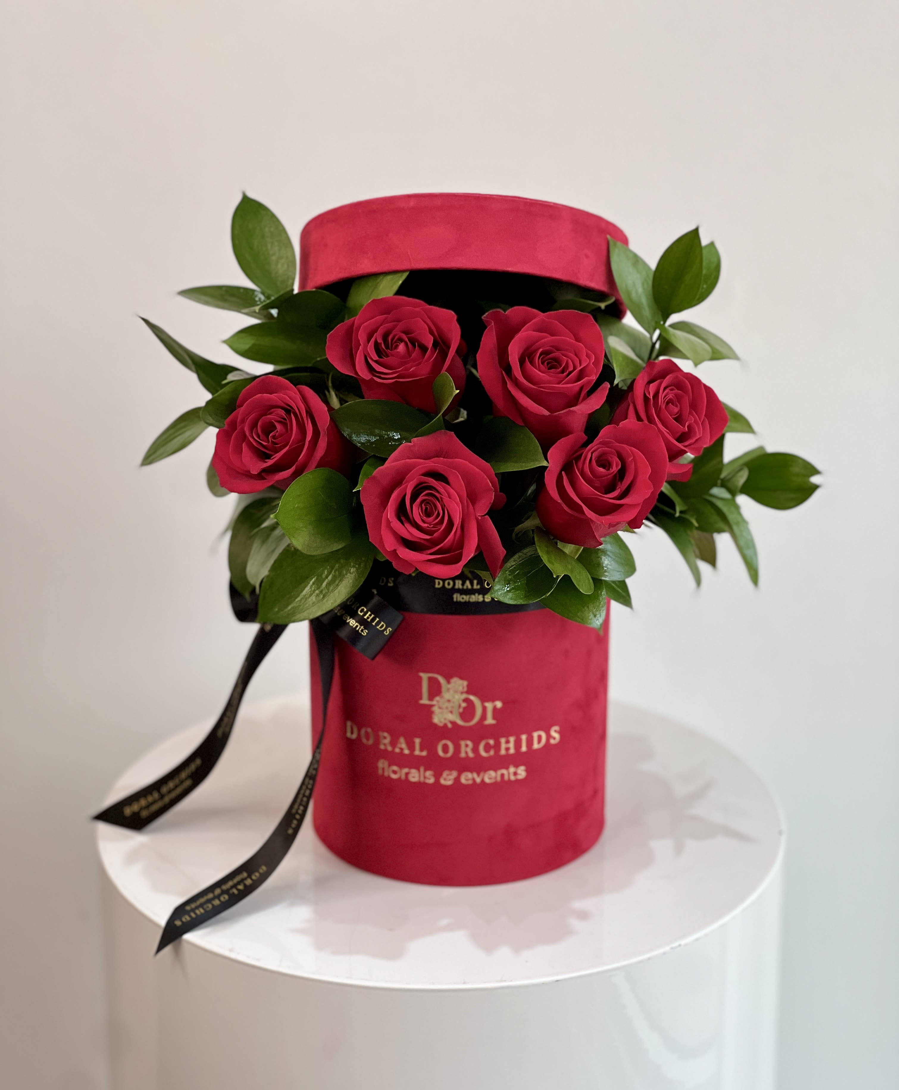 Amore - round box ™ - Elegant and timeless, this arrangement showcases velvety red roses surrounded by lush greenery. Set in a luxurious red velvet hatbox tied with satin ribbon, it radiates romance and sophistication.