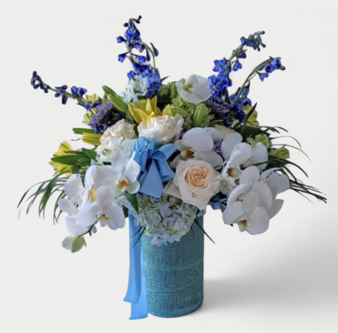 Blue Beautiful Bouquet Designer's Choice - Beautiful blue bouquet filled with roses orchids hydrangeas and more arranged in a tall modern glass cylinder vase wrapped in blue jute ribbon. Perfect to send today to make them smile. Always made extra special and unique each time. Send them happiness.