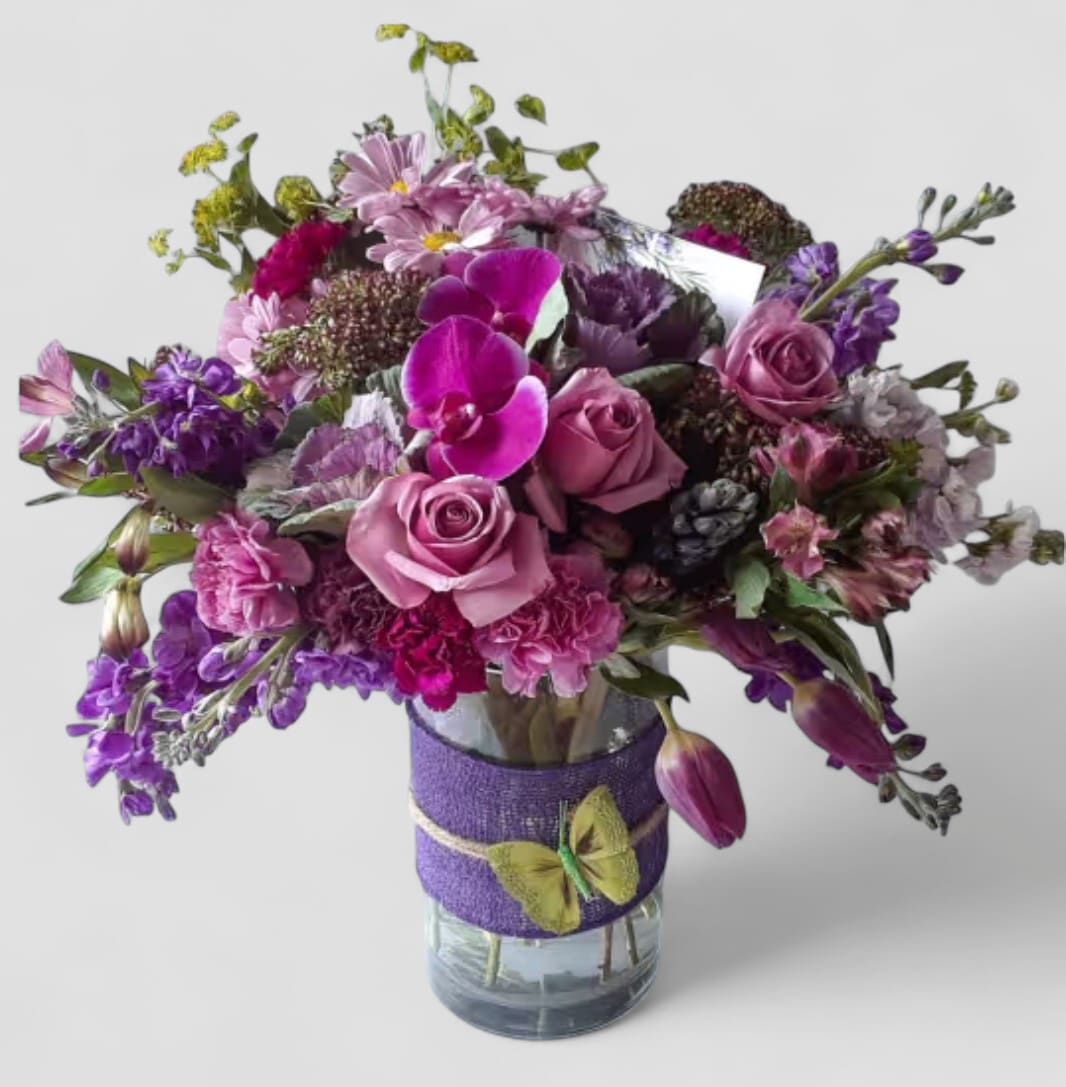 Purple Blossoms Condolences Designer's Choice - Roses and more arranged in a tall modern glass cylinder vase wrapped in purple jute ribbon. Beautiful and made unique each time. Please visit my beautiful gallery. Send them your deepest condolences.