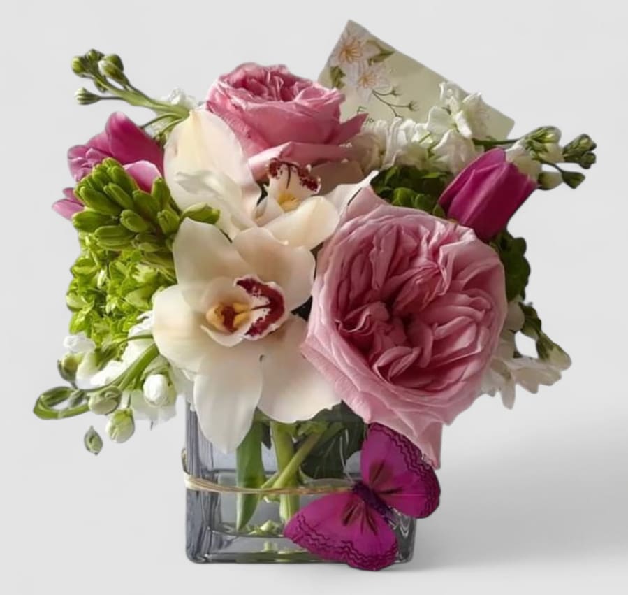Pink Rose Designer's Choice - Send this beauty today to make them smile with it's lovely pink and white blossoms of the day roses orchids and more arranged in a modern glass cube vase adorned with a sparkly cheery butterfly. Elegant and thoughtful. Always made extra special and unique. Send them happiness.