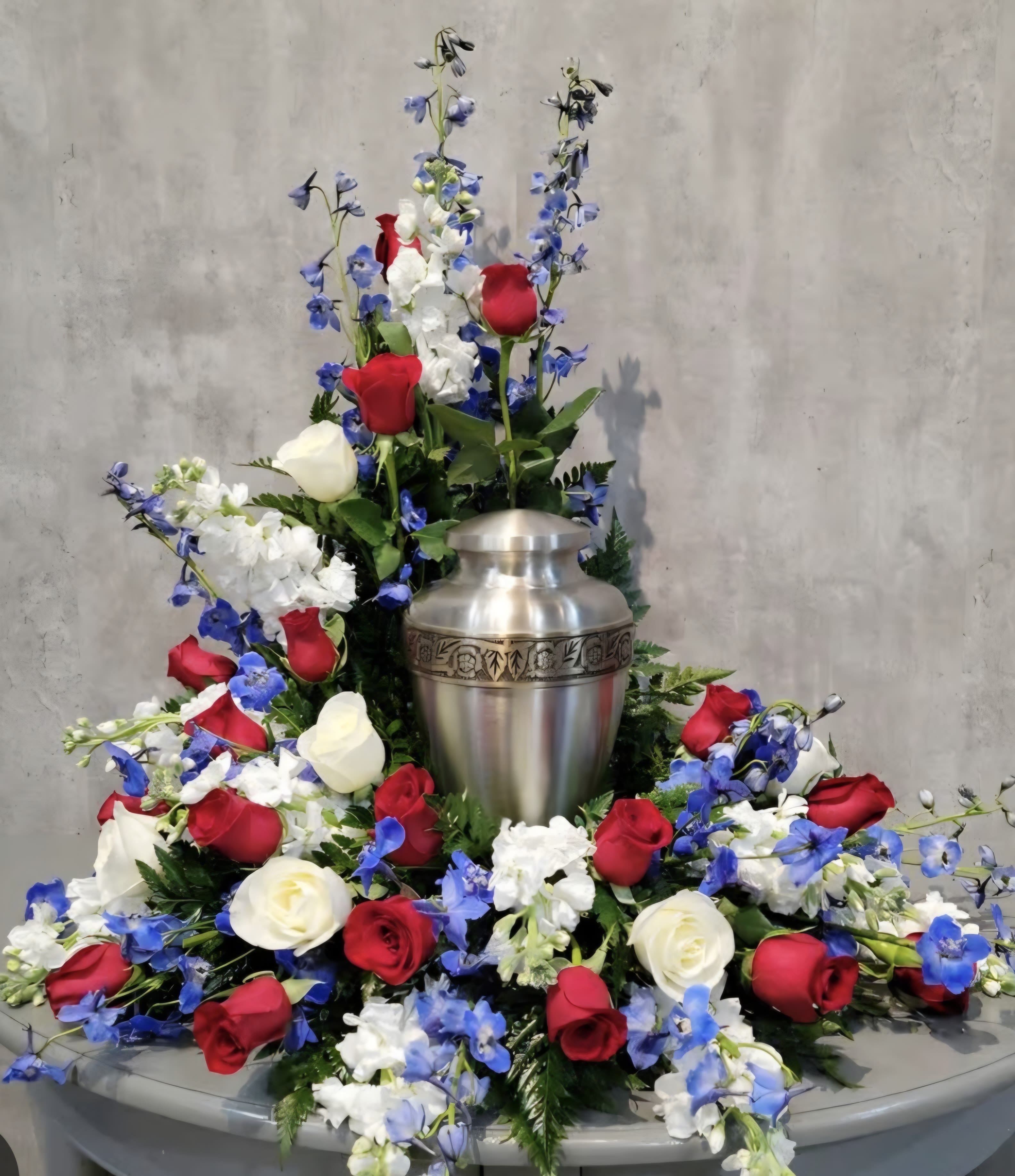 Patriotic Tribute - This red, white and blue pays tribute to a man/woman who has served. This beautiful arrangement swirls around the urn embracing love and compassion.