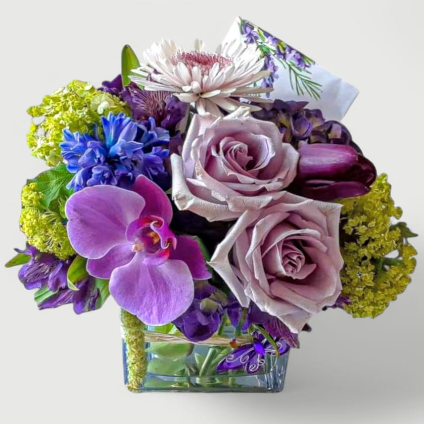 Lavender Mint Beauty Designer's Choice Lavender Mint Beauty Designer's Choice - Send this pretty bouquet today to make them smile with it's lovely mixed lavender and green blossoms of the day roses orchids and more arranged in a modern glass cube vase. Perfect to send for every reason. Always made extra special and unique each time. Send them happiness.