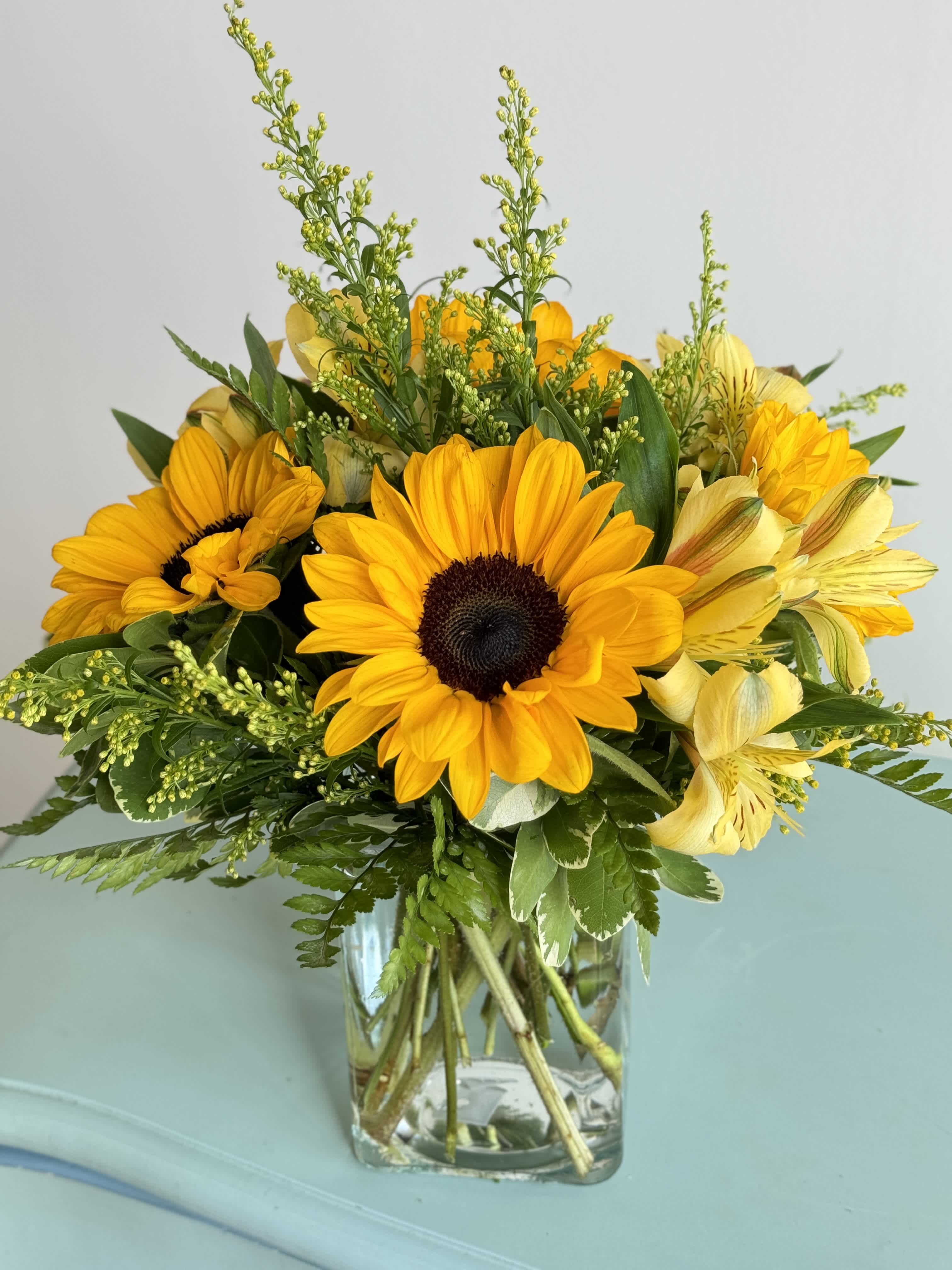 Sunny Days - Brighten someone’s day with bright yellow sunflowers accented with solidago and arranged in a chic clear vase.