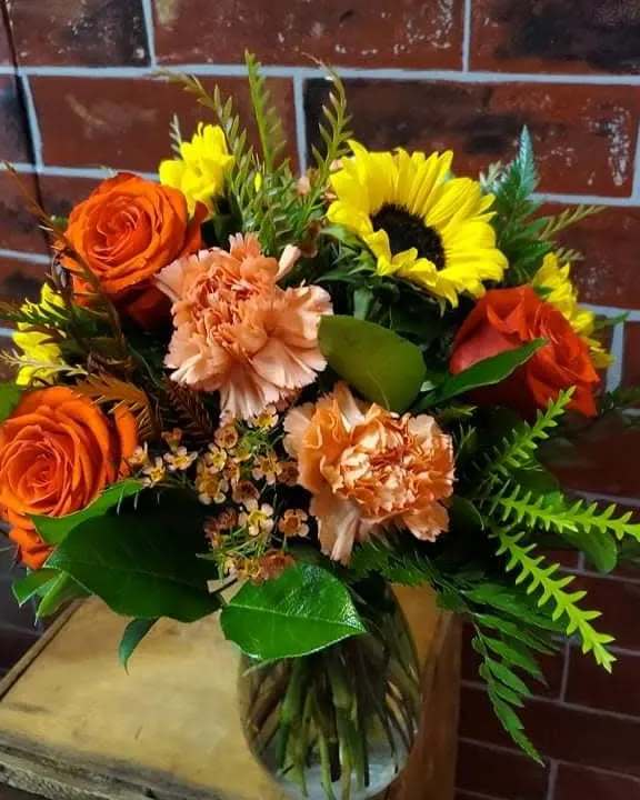 Simply FalI - An all around flower arrangement designed with fresh flowers to include mix of red and orange flowers to include sunflowers, roses, carnations, filler, and mixed greens in a vase.  * Some stages of flower life may vary. (Example: Lilies may be more open than imaged.) Flower shortages and product availability means that some substitutions will apply. Value will always be filled. This bouquet might include eucalyptus amongst the greenery. It may be toxic to pets including but not limited to Cats and Dogs if digested.