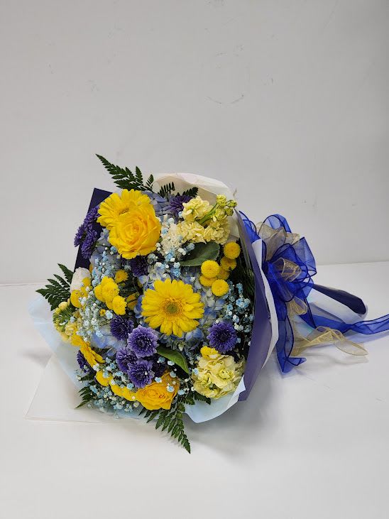 Blue Skies and Sunshine Cello Blue Skies and Sunshine Cello - A cheerful mix of golden yellow blooms, soft blue hydrangea, and deep purple accents wrapped with matching ribbons for a bold yet elegant finish. This arrangement brings the brightness of sunshine and the calm of blue skies all in one bouquet.