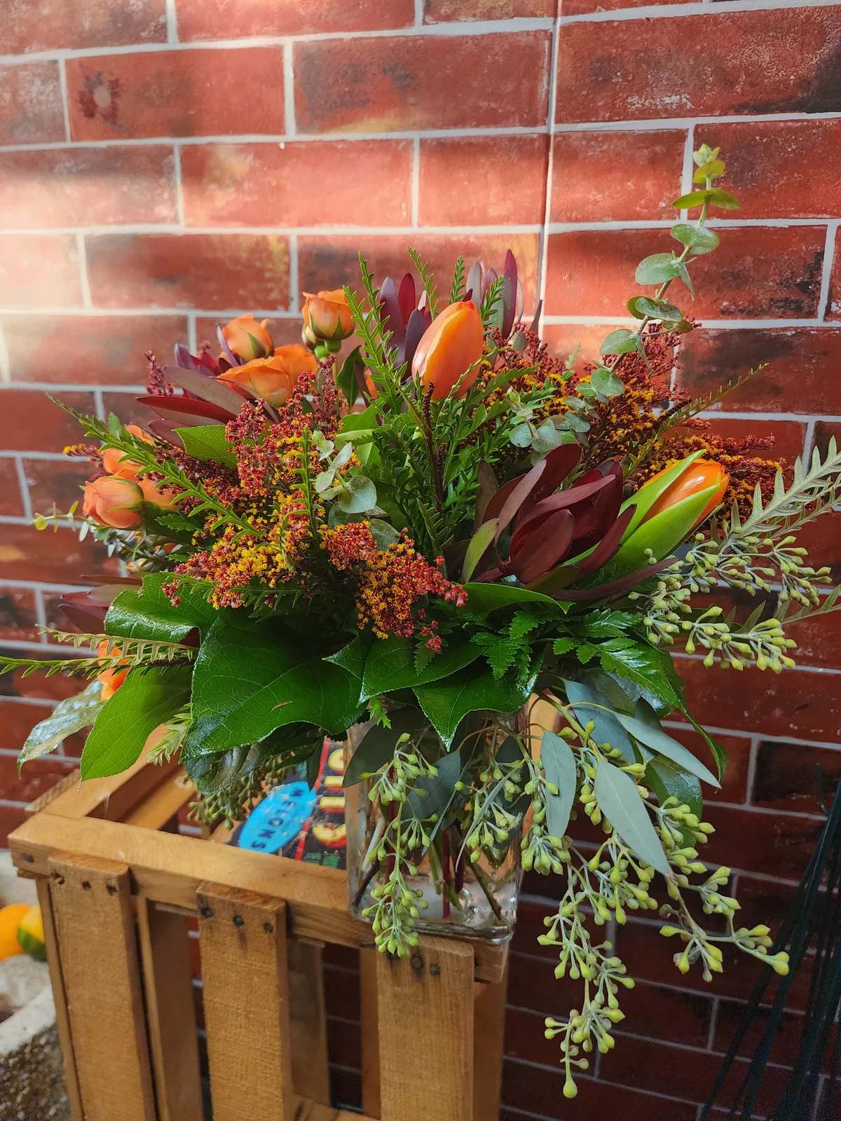 Celebrating Harvest - An all around flower arrangement designed with fresh flowers to include sunset safari, orange spray roses, orange tulips, tinted solidago, mixed greens in a vase.   * Some stages of flower life may vary. (Example: Lilies may be more open than imaged.)  Flower shortages and product availability means that some substitutions will apply. Value will always be filled. This bouquet might include eucalyptus amongst the greenery. It may be toxic to pets including but not limited to Cats and Dogs if digested.