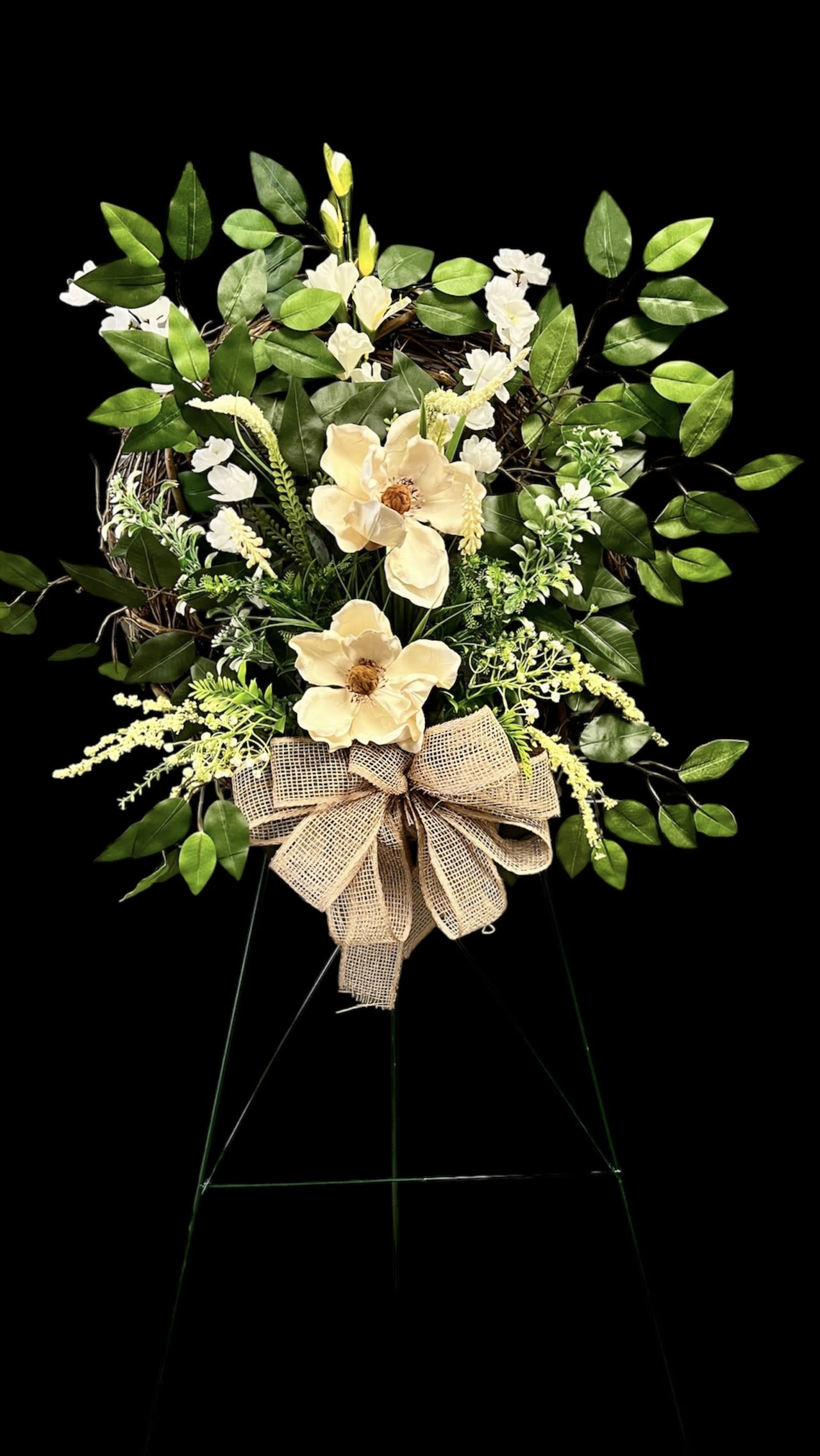 Eternal Magnolia Silk Tribute Stand - Honor a loved one’s memory with our Eternal Magnolia Tribute Stand, a graceful silk funeral arrangement designed for lasting beauty. Featuring lifelike magnolia blooms, soft ivory accents, and lush greenery, this standing spray conveys peace, strength, and timeless love. Finished with a rustic burlap bow, it offers a natural yet elegant touch for services, memorials, or a lasting keepsake for the family.