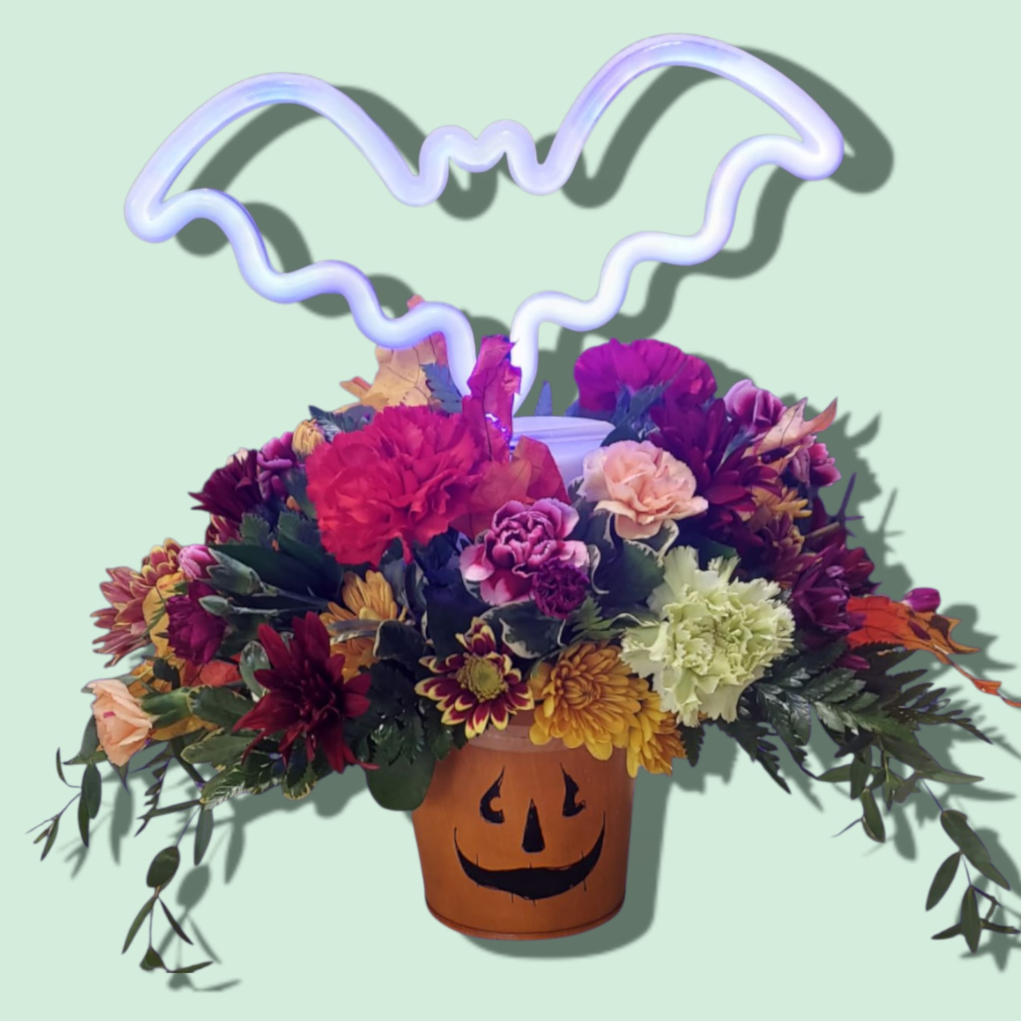 Hallow-Gleam - A jack-o-lantern tin is overflowing with autumn colored mums, carnations, mini carnations, and fall leaves. A keepsake neon table light is bursting through the blooms. LAMP SHAPES AND FLOWER COLORS WILL VARY WITH AVAILABILITY. LAMP INCLUDES BATTERIES AND A USB CORD. Over all arrangement size: 14&quot;H x 14&quot;L Lamp sizes: bat 11&quot; x 7.1,&quot; Pumpkin 8.5&quot; x 10,&quot; Ghost 7&quot; x 11.2,&quot; Cat 5.9&quot; x 9&quot;