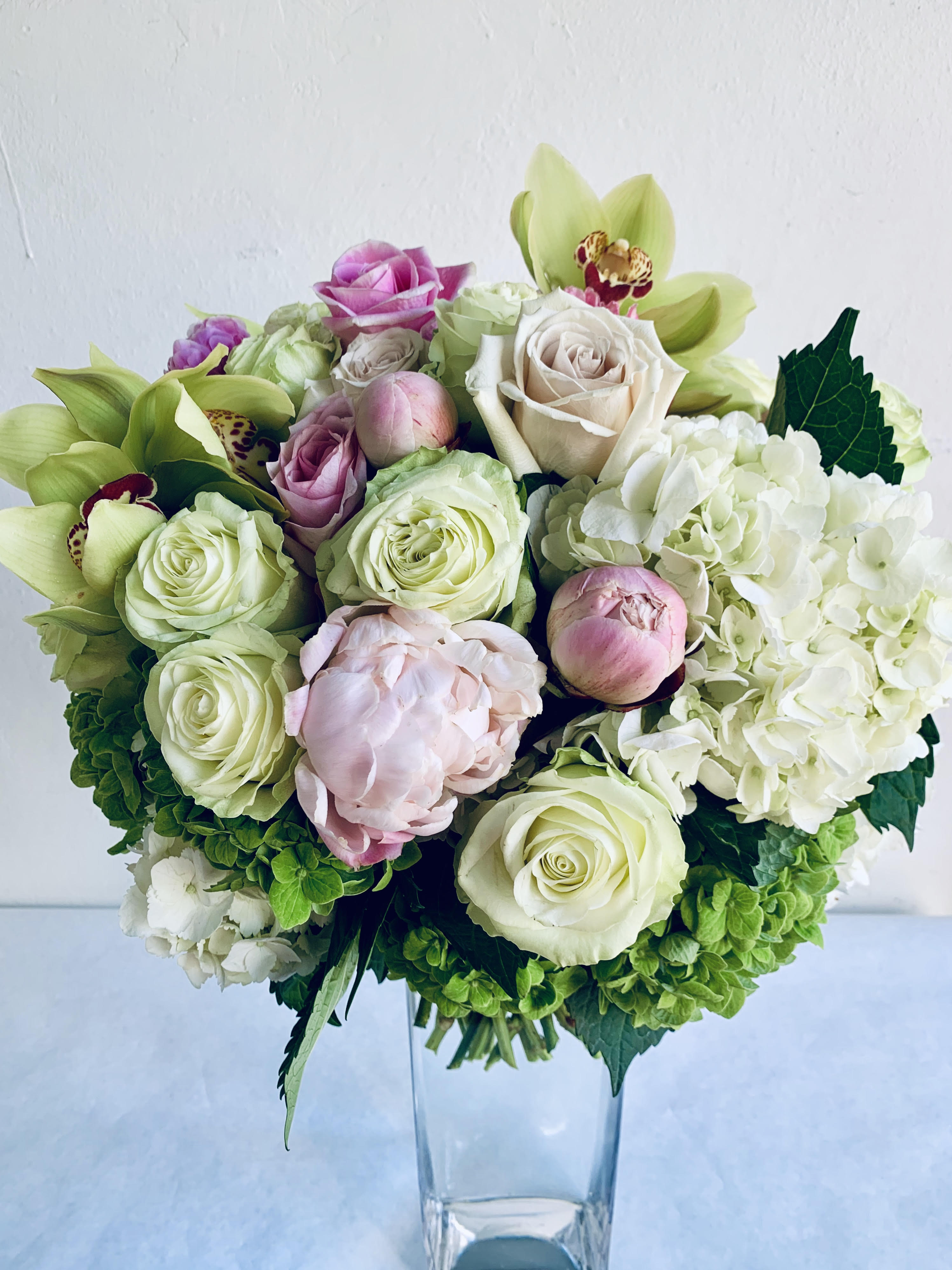 Magnolia - Pastel tones in shades of soft pinks and pale greens featuring an assortment of roses, spray roses green &amp; white hydrangeas and green cymbidium orchid  PHOTO - Deluxe 