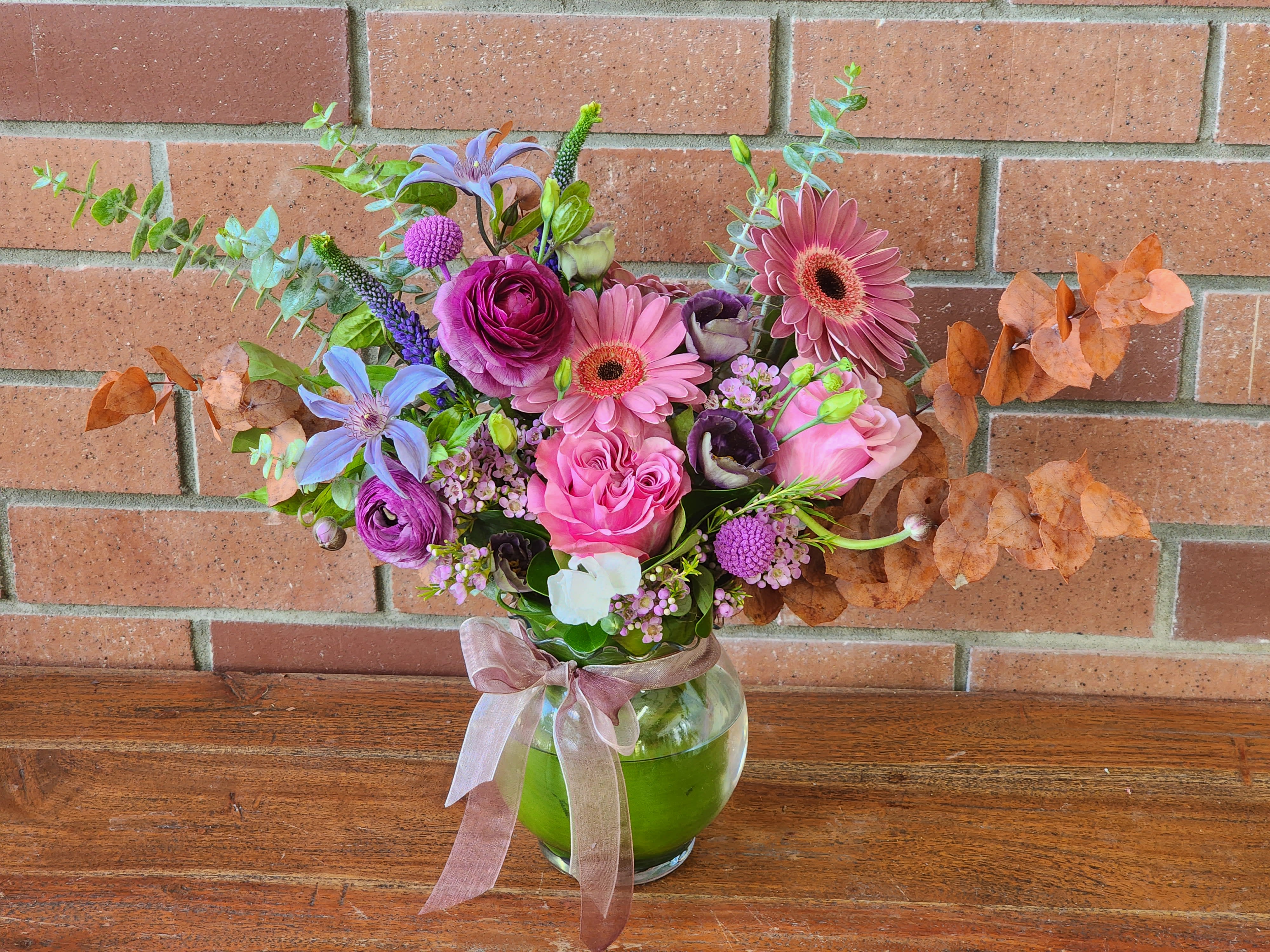 Berry Blooms Berry Blooms - Fresh arrangement in the Berry shades - gerbers, roses, ranunculus, Eucalyptus, lisianthus, wax flowers and more in a bubble bowl vase.