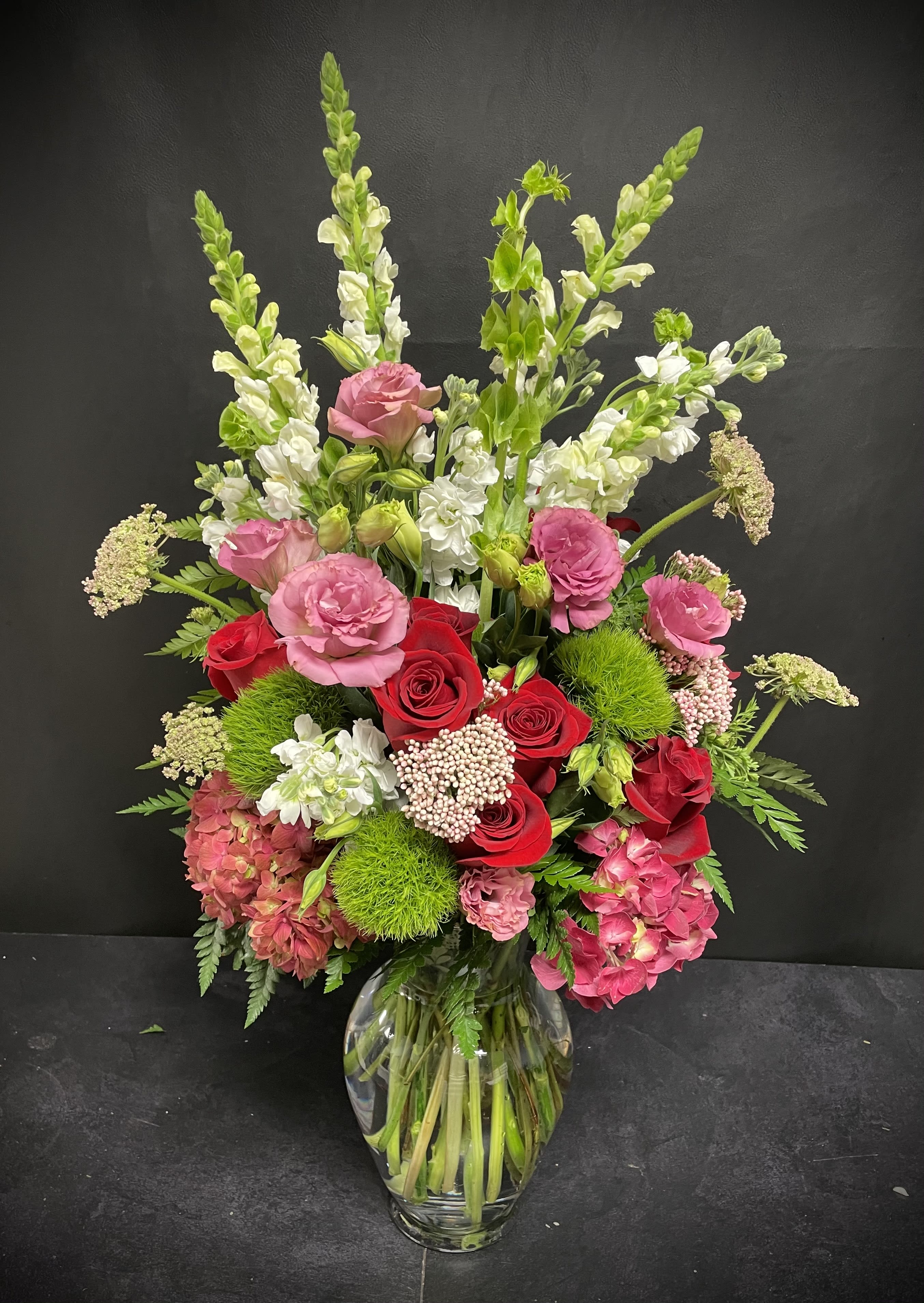 La Tour Eiffel La Tour Eiffel - Elegant and timeless, this striking arrangement is inspired by the grandeur of Paris itself. Deep red hydrangeas and classic red roses create a passionate foundation, softened by airy white snapdragons, white stock, and delicate queen Anne’s lace. Accents of bells of Ireland, green dianthus, pink lisianthus, rice flowers, and fragrant eucalyptus add layers of texture and sophistication. A true statement piece — bold, romantic, and unforgettable.