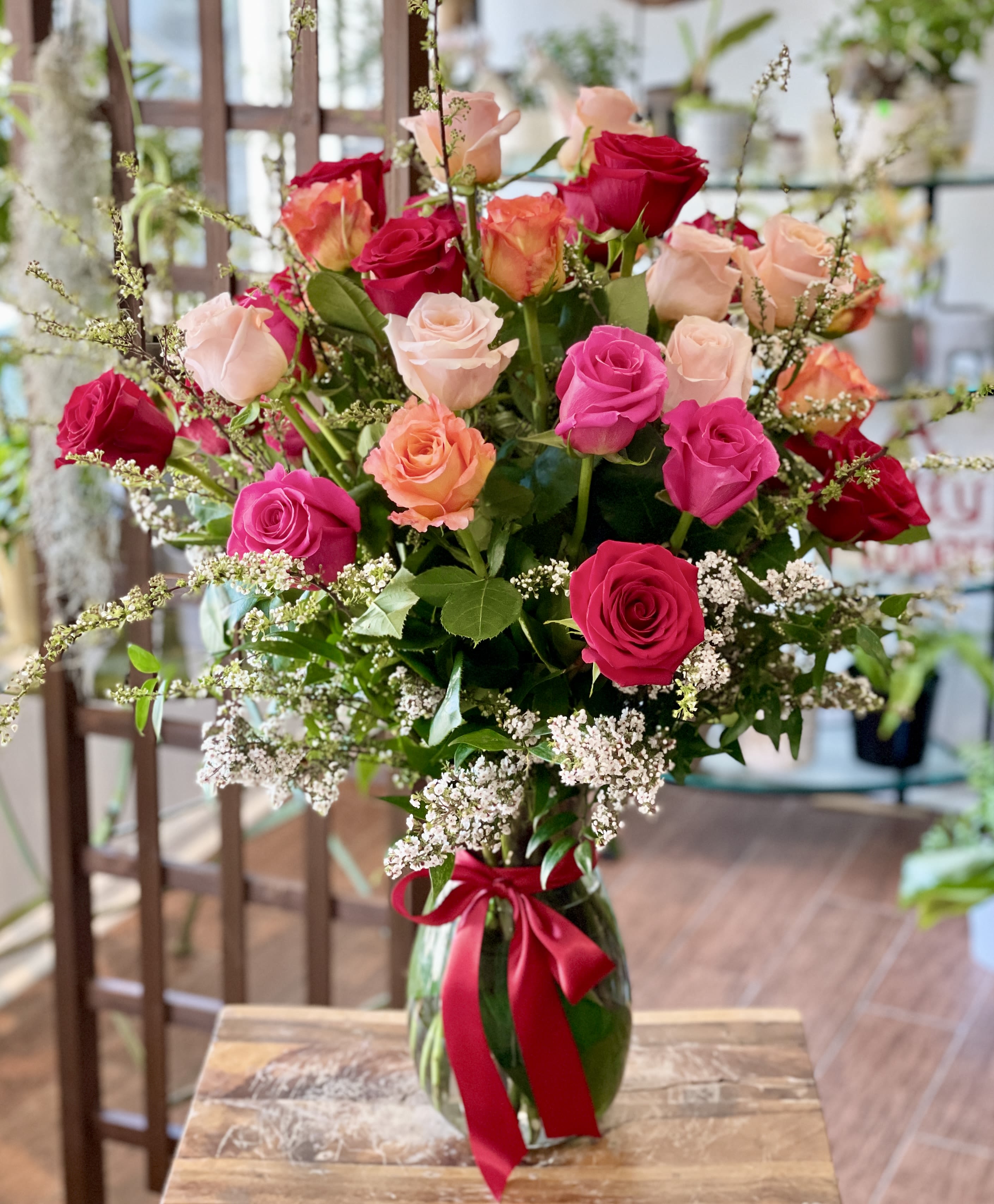 Adaline - 36 roses in a variety of colors with seasonal accents and foliage, arranged in a tall design within a clear glass vase.