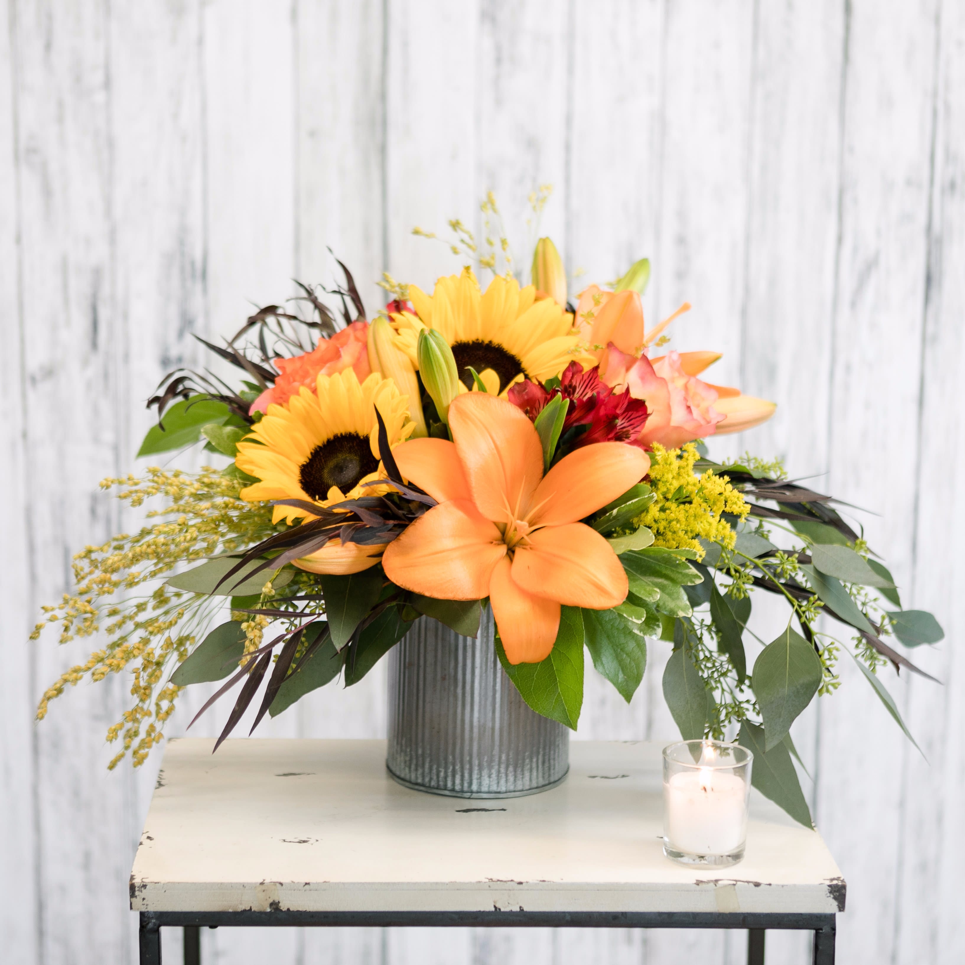 Bounty - Overflowing with autumn favorites including lilies, eucalyptus, roses and sunflowers, this rustic metal vase arrangement is the perfect choice to add fall color to the office, dorm or kitchen table!