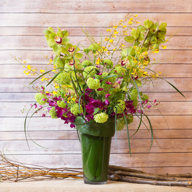 GARDEN OF ORCHIDS GARDEN OF ORCHIDS - VASE LINED WITH TI LEAF, LOOSELY ARRANGED WITH CYMBIDIUM, ONCIDIUM, DANDROBIAN ORCHIDS, AND A BACKGROUND OF VIBURNUM AND BEAR GRASS.