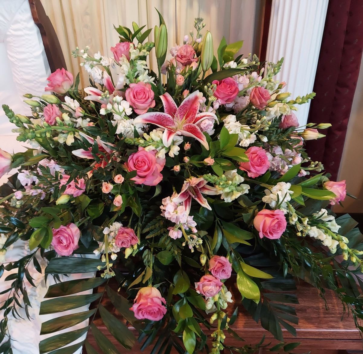 Casket Spray CS-34 Casket Spray CS-34 - This feminine casket spray offers a graceful and heartfelt tribute, blending soft pink roses, stargazer lilies, snapdragons, and delicate seasonal blooms. Designed with flowing greenery and lush texture, it conveys admiration, love, and a gentle farewell. A beautiful expression for honoring a cherished mother, sister, daughter, or dear friend.