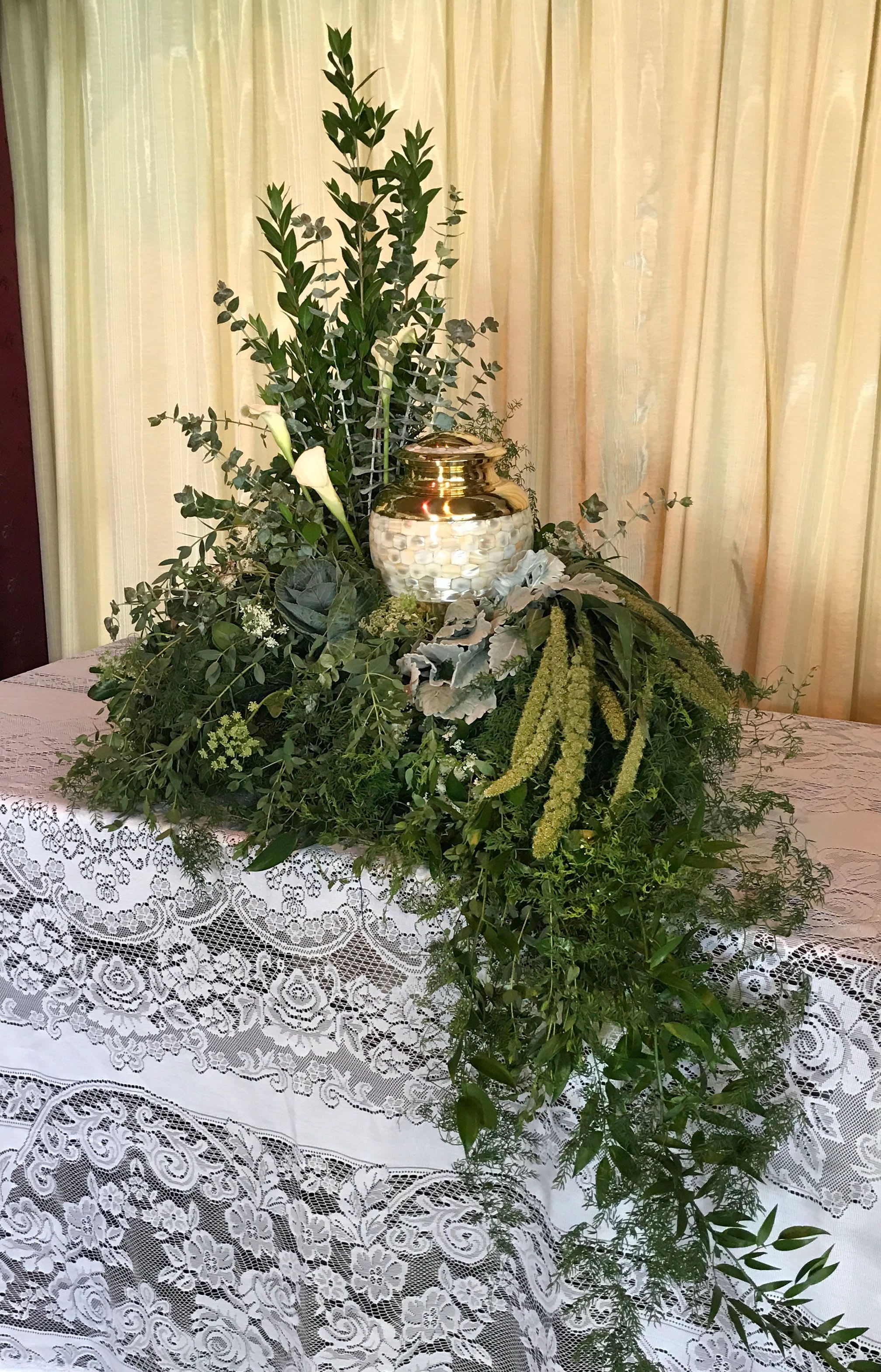 Memorial Spray MS-04 Memorial Spray MS-04 - Natural and understated, this lush greenery-focused memorial spray offers a peaceful, organic tribute. Layers of textured foliage—including eucalyptus, ruscus, dusty miller, and cascading amaranthus—surround the urn with quiet beauty. Accented with ivory calla lilies for a touch of purity, this arrangement creates a serene and grounded presentation, honoring a loved one with timeless grace and a connection to nature. (Urn not included)