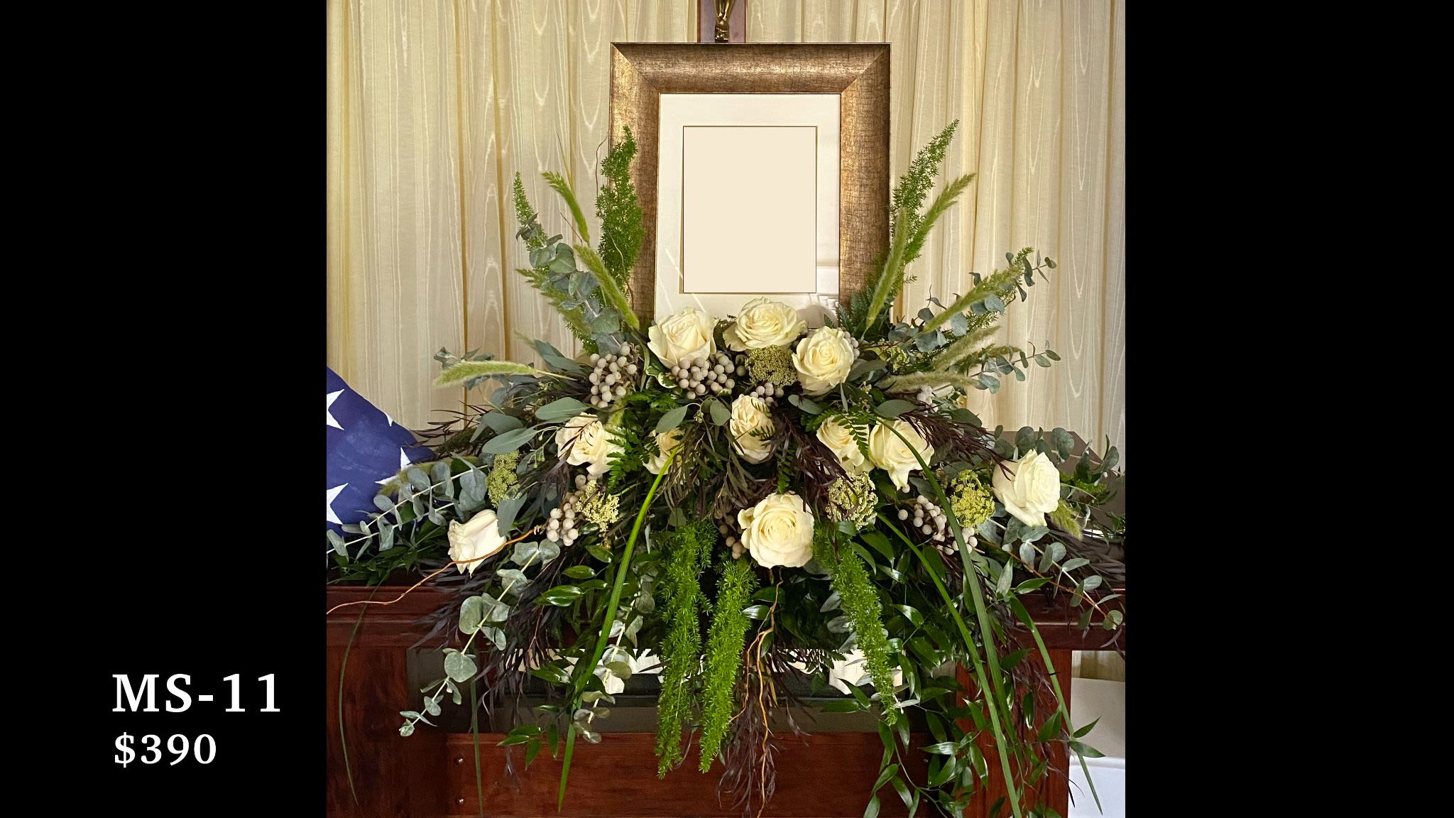 Memorial Spray MS-11 Memorial Spray MS-11 - A refined and natural tribute, this photo memorial spray features creamy white roses, snowberries, and Queen Anne’s lace nestled among textured greenery, eucalyptus, and cascading amaranthus. The neutral tones and organic styling evoke a quiet strength and timeless dignity. Designed to frame a cherished photograph, this arrangement offers a graceful expression of remembrance and honor—especially fitting for a veteran or someone deeply connected to nature. (Picture frame and flag not included)