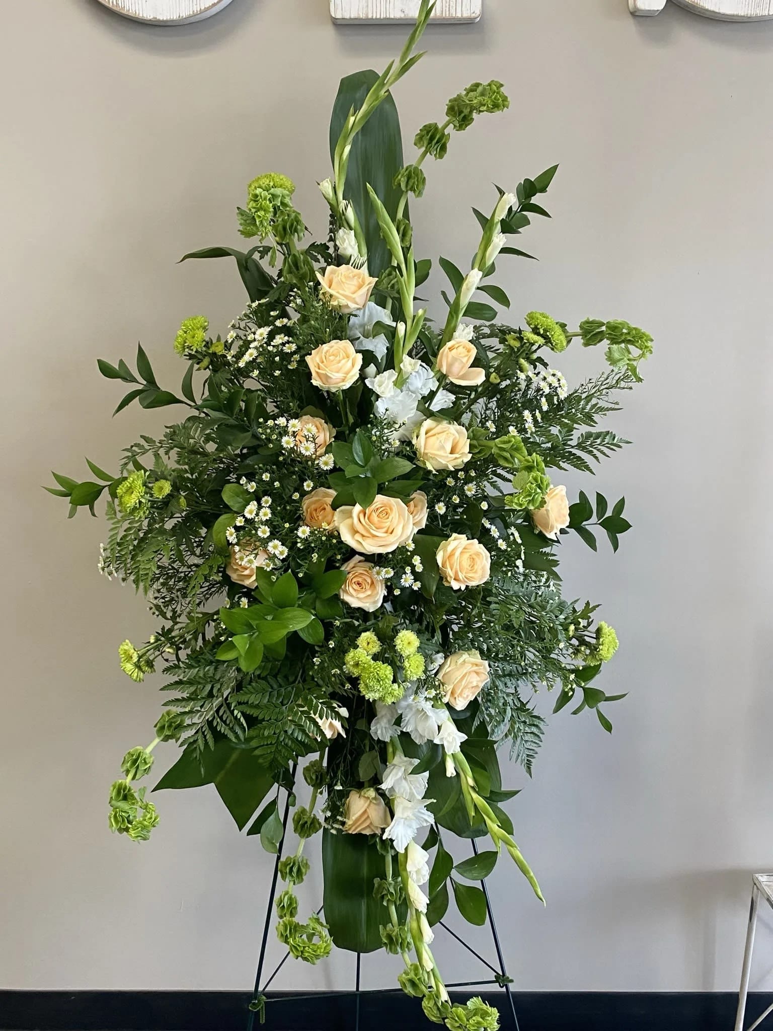 Easel Spray ES-21 Easel Spray ES-21 - Soft peach roses, white gladiolus, green trick dianthus, and miniature daisies create a peaceful and refined display in this standing spray. Lush greenery and flowing lines bring balance and movement to the design, making it a thoughtful expression of remembrance. Easel stand included.
