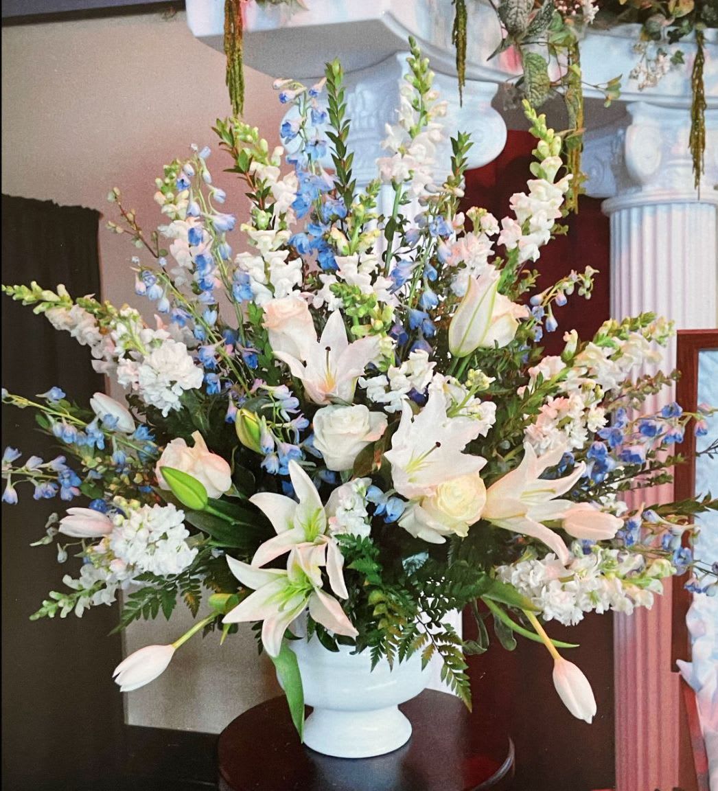 Ceremony Arrangement CV-10 Ceremony Arrangement CV-10 - Soft and uplifting, this ceremony arrangement features white lilies, roses, snapdragons, tulips, and light blue delphinium. Set in a pedestal container, its gentle palette of ivory and blue offers a peaceful and graceful tribute, ideal for honoring a loved one with beauty and compassion.