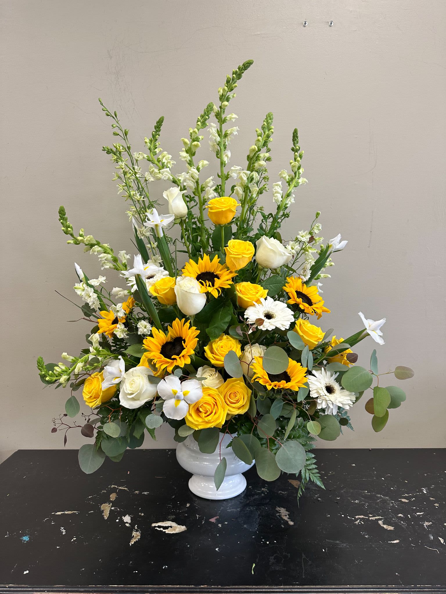 Ceremony Arrangement CV-21 Ceremony Arrangement CV-21 - Radiating warmth and comfort, this uplifting design features bright sunflowers, yellow and white roses, snapdragons, daisies, and soft eucalyptus accents. Created in a pedestal-style container, this arrangement brings a sense of hope and light to the service, honoring a life remembered with joy and gratitude.