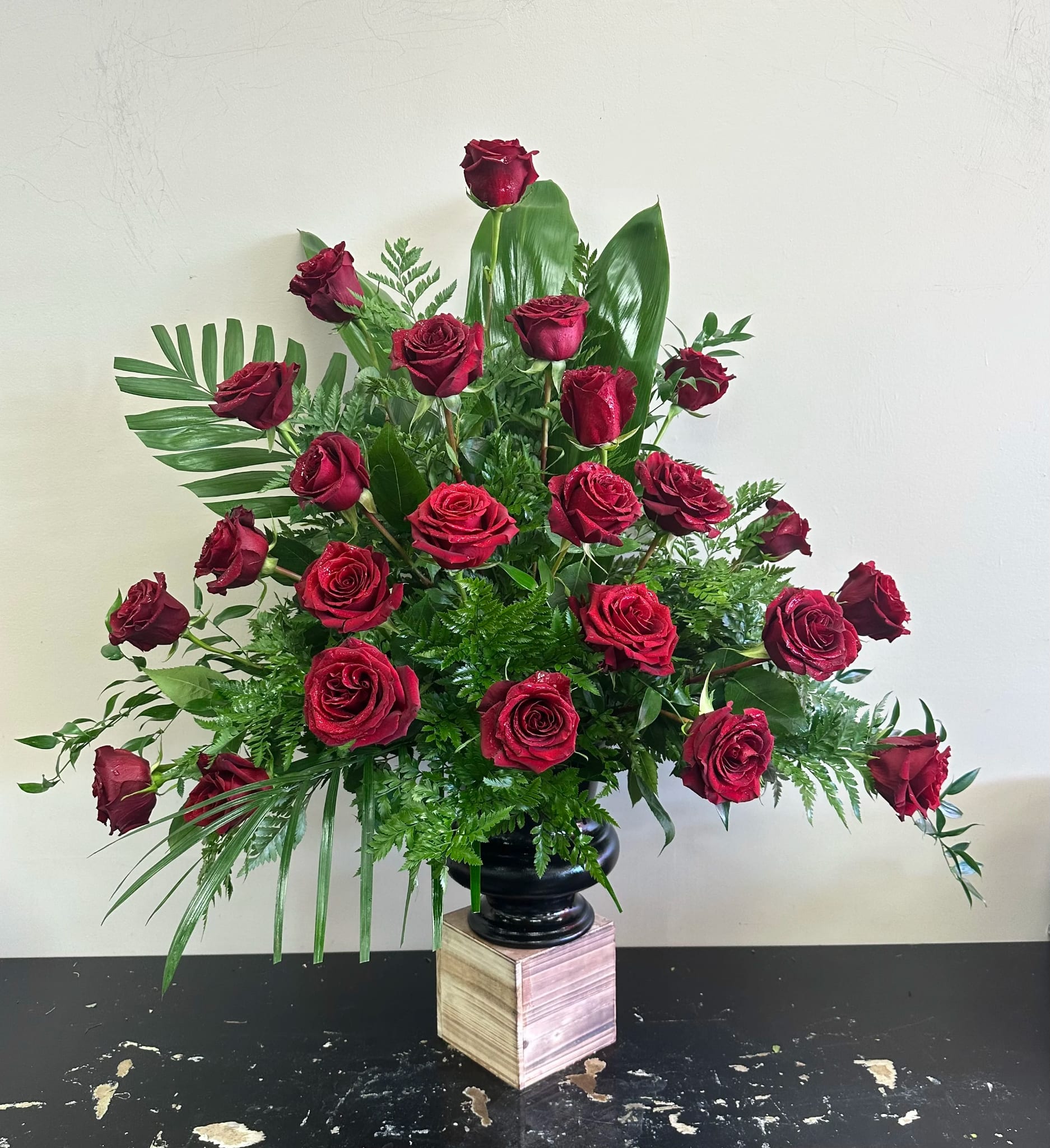Ceremony Arrangement CV-25 Ceremony Arrangement CV-25 - A timeless gesture of love and remembrance, this ceremony arrangement features rich red roses arranged in a lush fan of tropical greenery. Bold yet graceful, it offers a striking visual tribute, symbolizing devotion, respect, and heartfelt farewell. Arrangement can be made with your choice of a single color of rose, please indicate if you would like red, white, yellow, soft pink, bright pink, purple or orange. Designer urn comes in white, black or bronze.