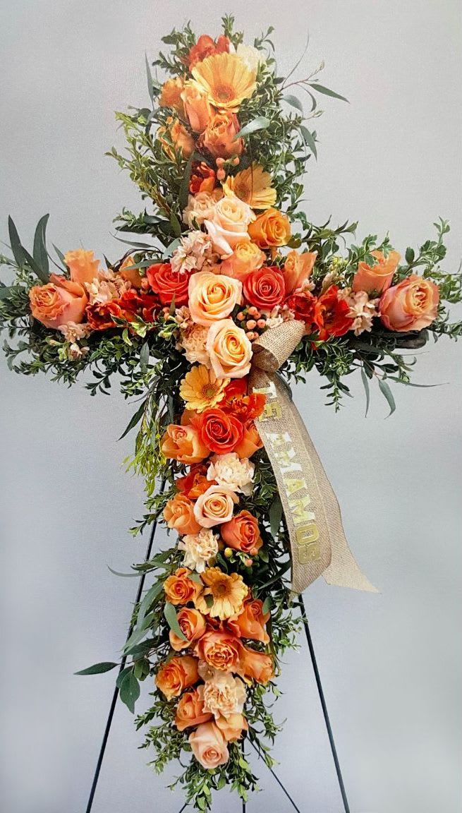 Cross CR-05 Cross CR-05 - A heartfelt tribute in warm sunset tones, this standing cross is filled with peach, orange, and apricot roses, accented by creamy carnations and soft greenery. Its natural and graceful style offers a message of peace and remembrance. Easel stand included. Ribbons available for an additional $10 per word.