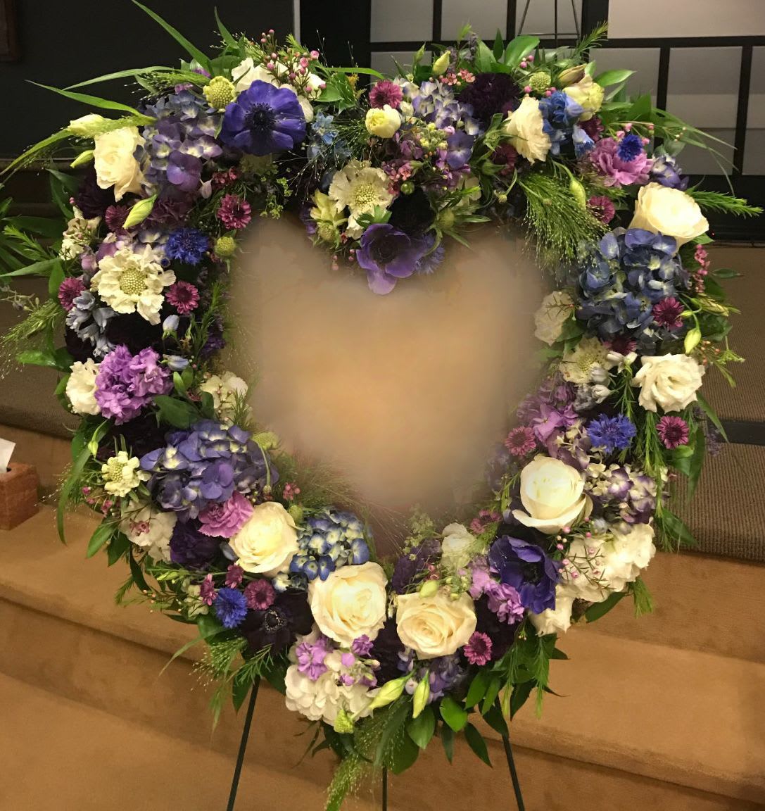 Heart HS-03 Heart HS-03 - A touching tribute filled with soft ivory roses, hydrangea, and rich purple blooms, this heart-shaped standing wreath is designed to honor a life with grace and beauty. With layered textures and hues of lavender, plum, and blue, it’s a meaningful choice for memorials in Verrado, Estrella Mountain Ranch, and surrounding Goodyear neighborhoods. Easel stand included; ribbon lettering is available for $10 per word.
