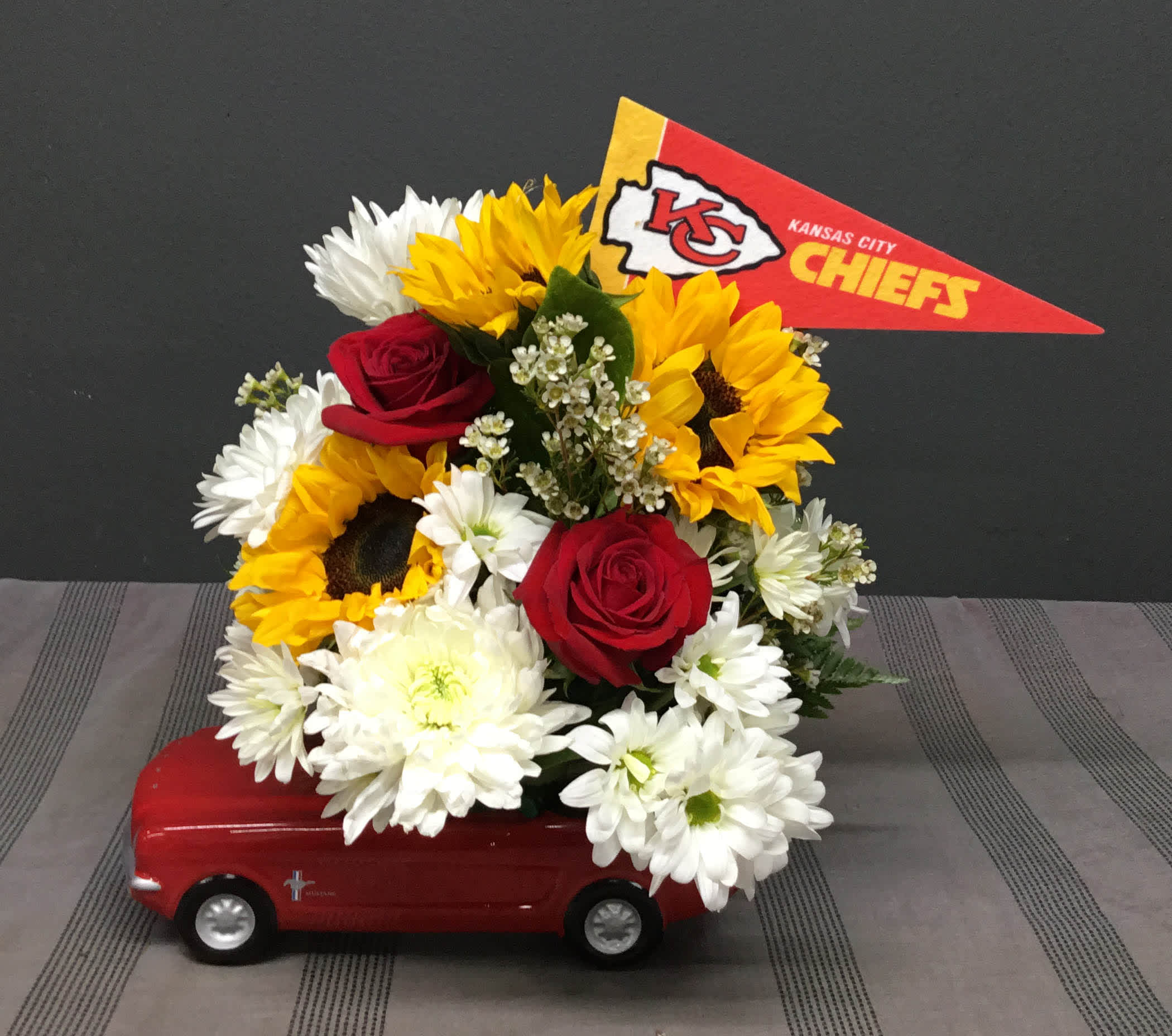 Chief's Ralley Chief's Ralley - Assorted Red, Yellow and White flowers with a Chief's Flag in a Ceramic Red Mustang.