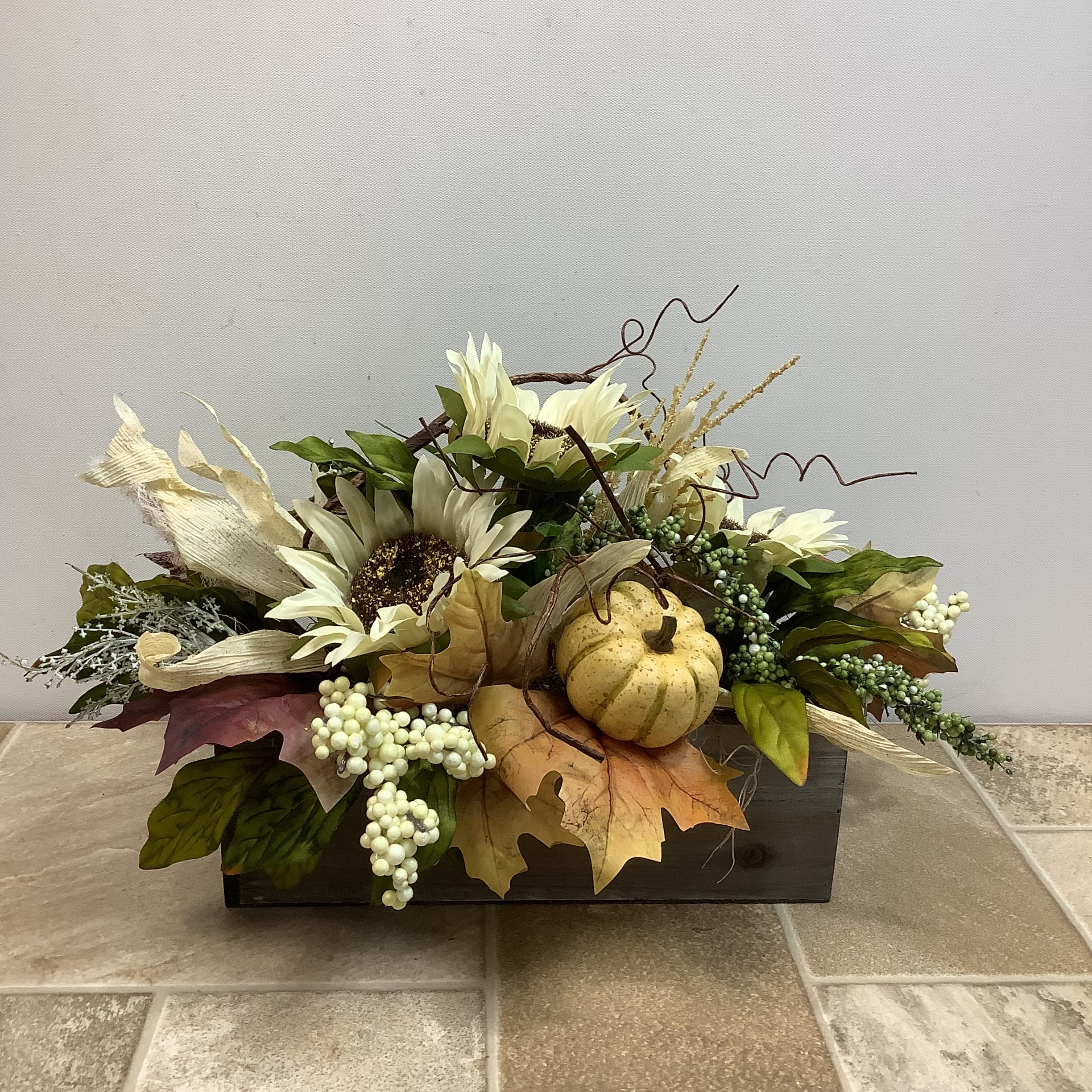 Artificial Fall Centerpiece Artificial Fall Centerpiece - This artificial flower arrangement is filled with a lovely collection of autumn favorites. Pumpkins, sunflowers, leaves and berries are artistically gathered in a gray wooden box. The overall size is 19” long x 11” high & wide.