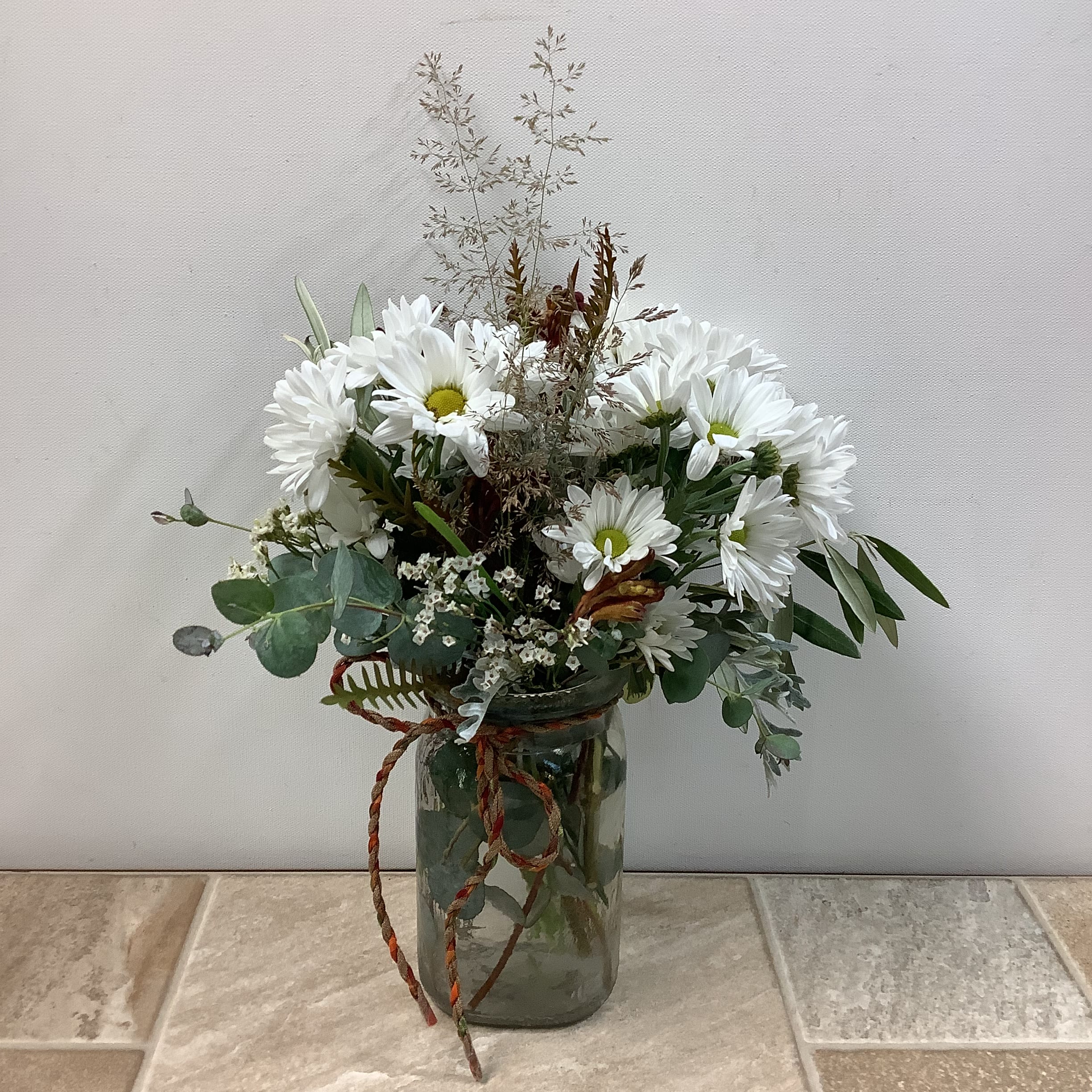 Cool Breeze Cool Breeze - "Cool Breeze" is a lovely arrangement of white daisies in a hammered glass mason jar vase, accompanied by white accent flowers and a variety of lush greenery. A charming length of twine around the jar adds to the natural look. Primary flower: daisy
