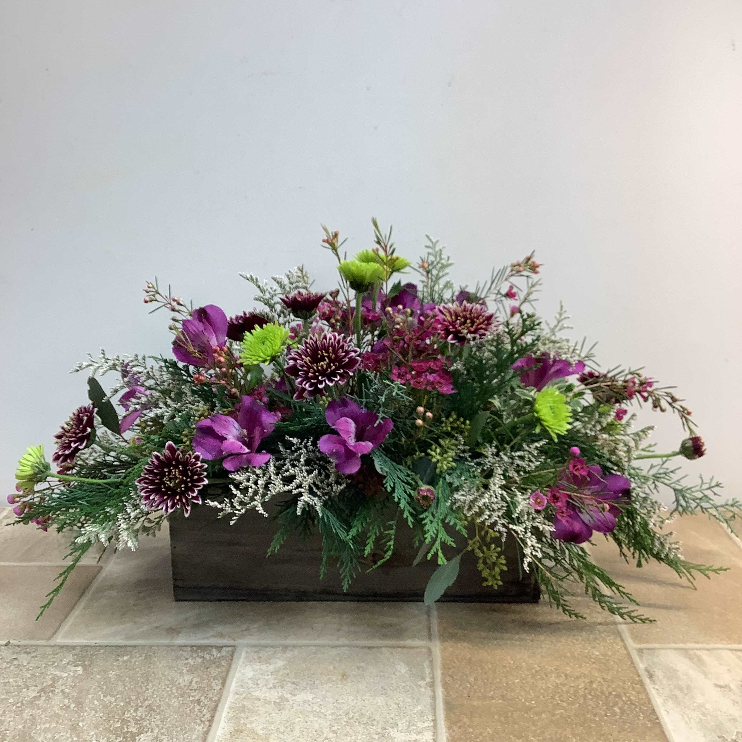 Country Garden - Reminiscent of a blooming countryside, this is an eye-catching long and low arrangement designed in a charming wooden box.  It’s filled with bi-colored purple chrysanthemums, purple alstroemeria, green button poms, misty white limon and wax flower.  Approximate size: 16” long x 10” high.   Primary flowers: mum, chrysanthemum, lily