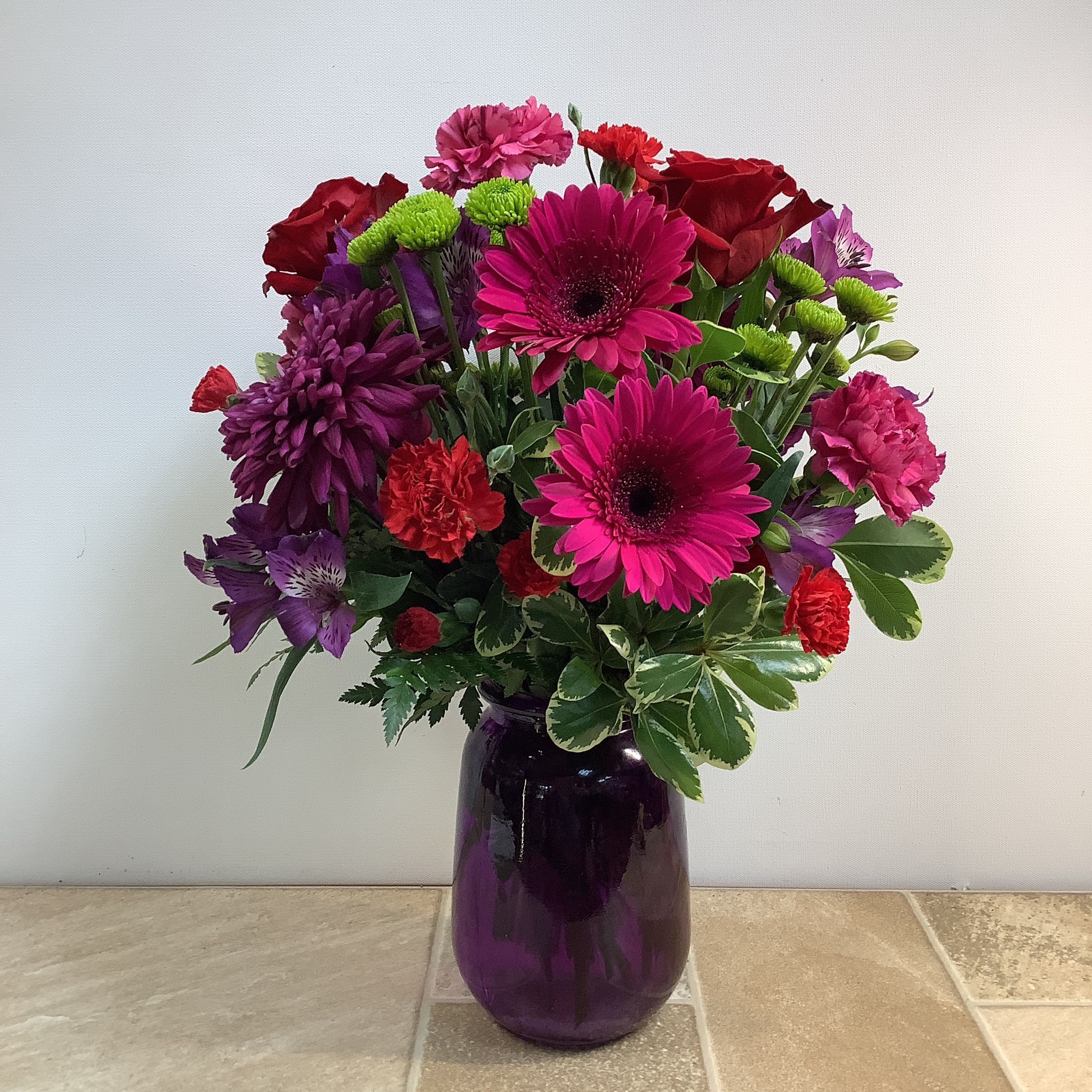 Especially For You Especially For You - This vibrant and full floral arrangement is presented in a purple vase and features a rich mix of flowers in shades of pink, fuchsia, red, and purple, complemented by green accents. Bright pink gerbera daisies give a bold pop of color, red roses add an elegant touch, ruffly red and pink carnations and lush purple cremones offer texture, and sweet purple alstroemeria rounds out this bold and beautiful bouquet. Approximately size: 14” wide x 19” tall. Primary flowers: daisy, rose, chrysanthemum, lily