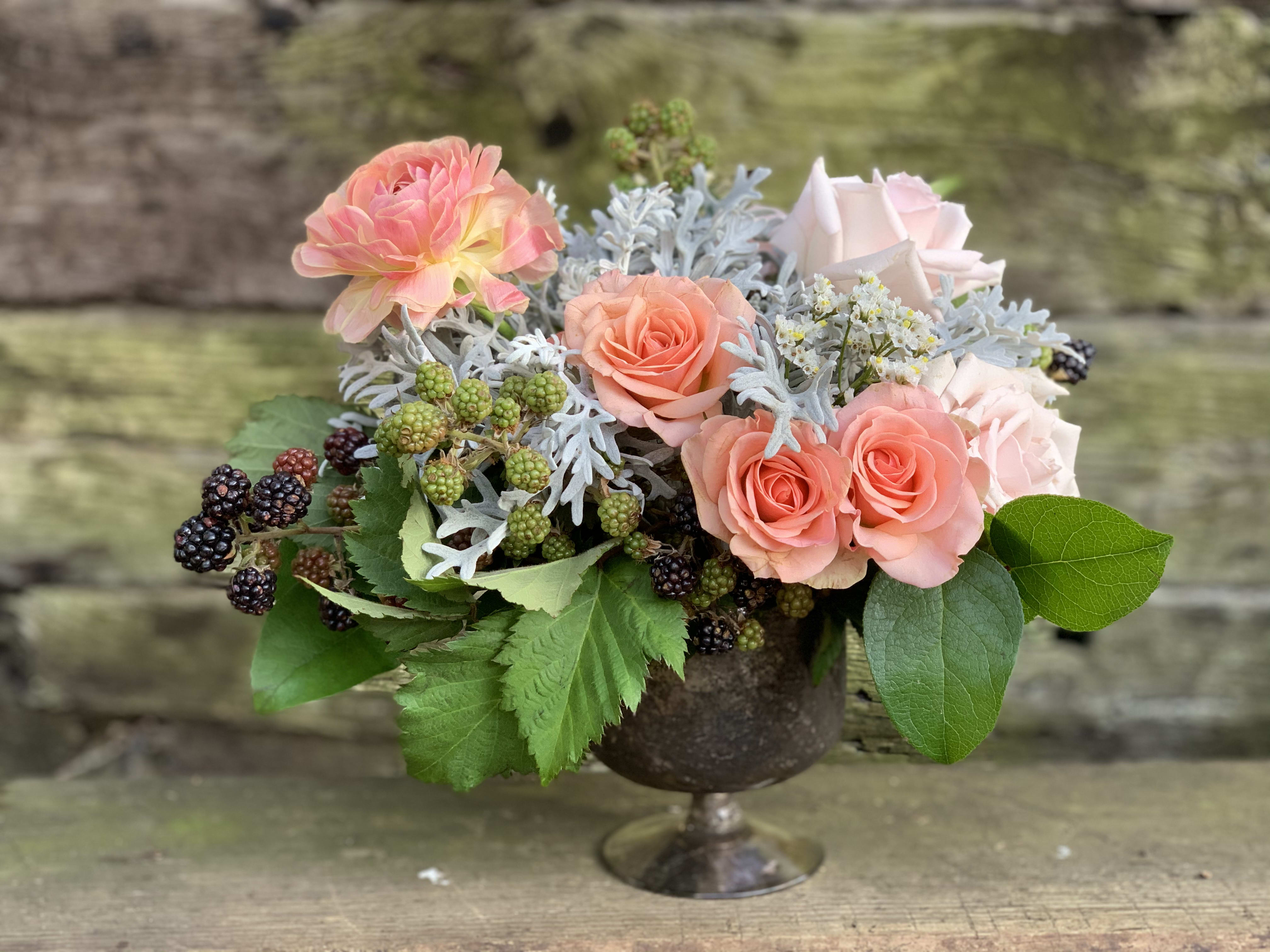 Zoe - Footed bowl filled with soft pinks and peachy, coral tones complimented in a bed of artemisia with accents of wild blackberries.  