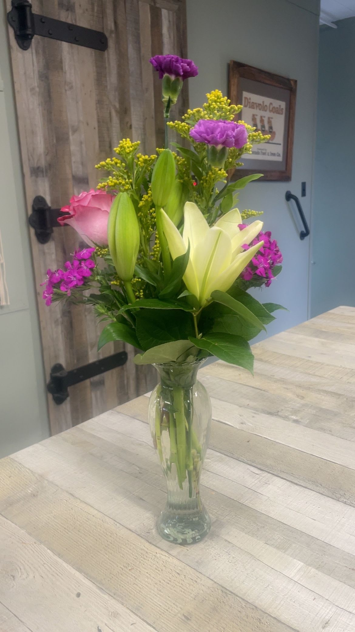 Everything Nice - A tall recycled glass contemporary vase with a lily, a rose, carnations and  filler. Just the right size to say “ Hey, I Love You” or “Great Job “or “Wow! You’re Awesome “. This arrangement is one sided. 
