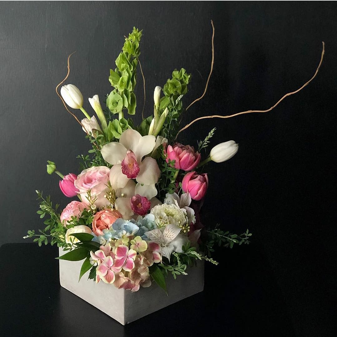 Spring Delight  - A vertical design with seasonal spring flowers in pastel mix Flowers may vary from hydrangeas,  cymbidum orchids tulips,  Roses spray Roses bells of Irelen curly willow, dusty miller, eucalyptus  wax flower,   ranunculus 