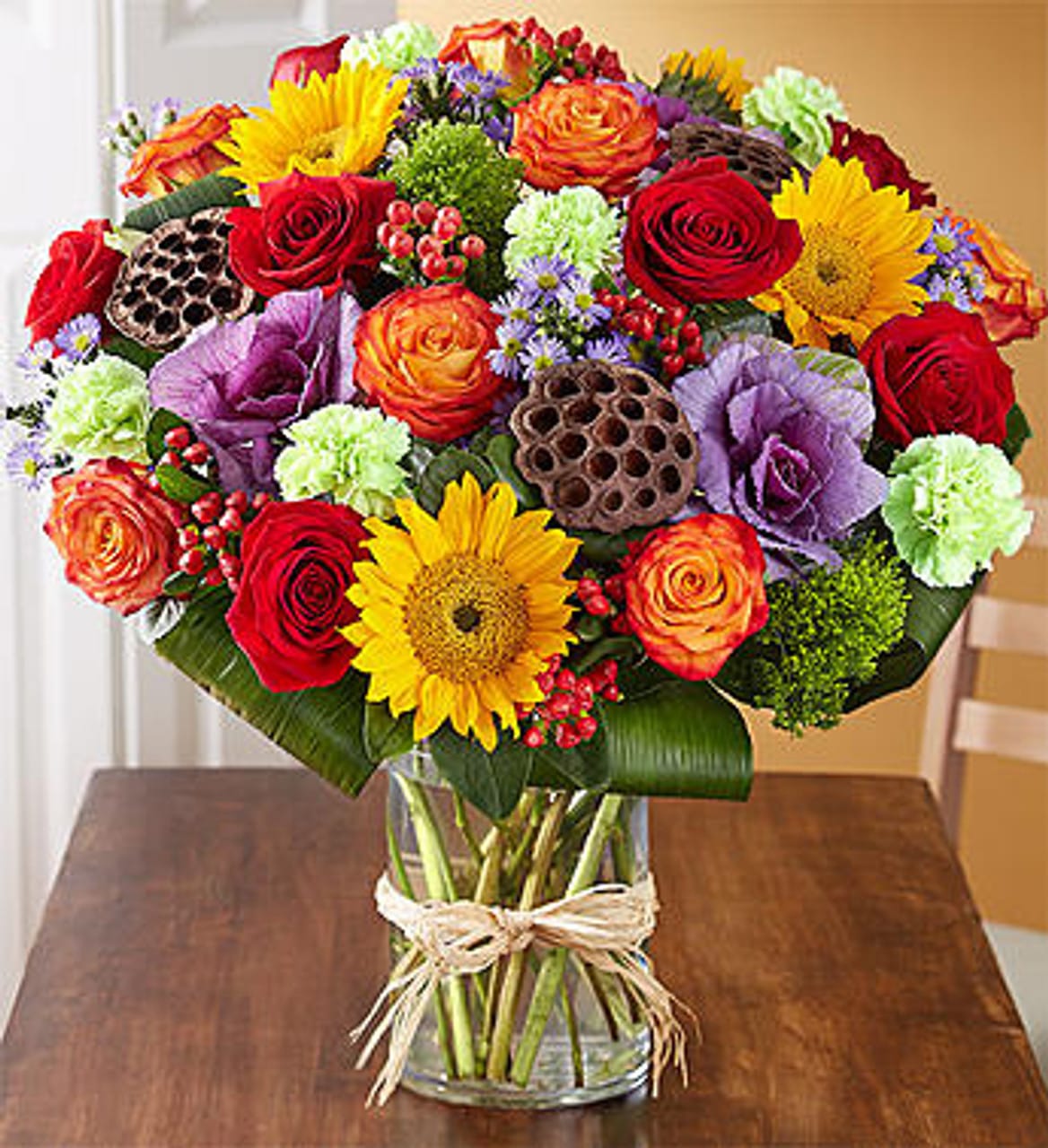 Garden Of Grandeur For Fall Garden Of Grandeur For Fall - We've taken one of our best-selling bouquets and filled it with all the rich colors and textures of fall. Radiant roses and sunflowers are hand-gathered with a mix of brightly colored blooms and unique accents inside a chic glass cylinder vase. Our vibrant arrangement is sure to delight at every festive gathering. All-around arrangement of red roses and hypericum; circus or bi-color orange roses; sunflowers; lime green carnations; and purple kale and monte casino; accented with greenery and dried lotus pods Artistically designed in a clear glass cylinder vase tied with raffia; measures 8"H Large arrangement measures approximately 22"H x 16"L Medium arrangement measures approximately 21"H x 15"L Small arrangement measures approximately 20"H x 14"L