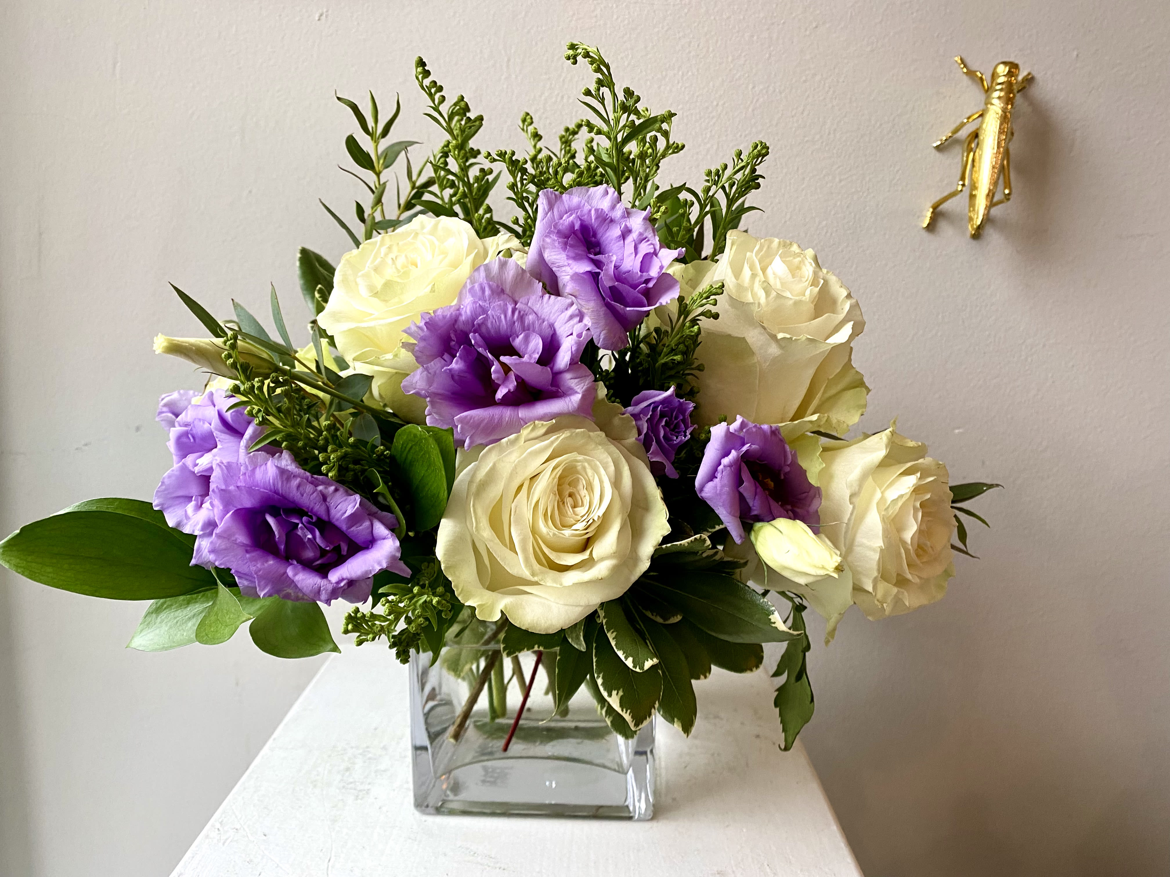 Petal Poetry  - A Low Elegant Centerpiece of 5 open white roses, specialty lisianthus (or lavender stock), solidago, accent flowers and greens.