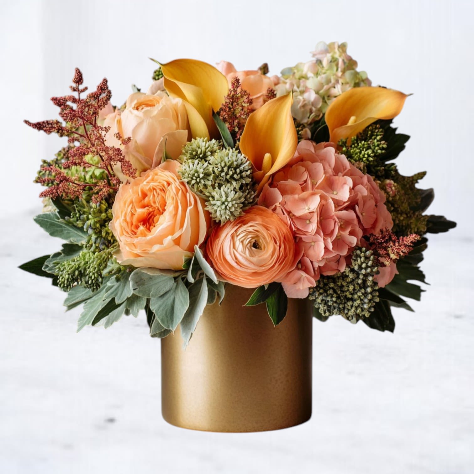 Gilded Ember Bouquet - Elevate your fall floral gifting with our Gilded Ember Bouquet, a luxurious arrangement designed for golden autumn moments. Featuring peach ranunculus, coral hydrangea, golden calla lilies, and premium garden roses, this bouquet radiates warmth and sophistication. Perfect for Thanksgiving centerpieces, fall weddings, or as a memorable gift, it brings the rich glow of the season into any space. Hand-delivered in a chic gold vase, this design blends modern elegance with timeless seasonal charm.