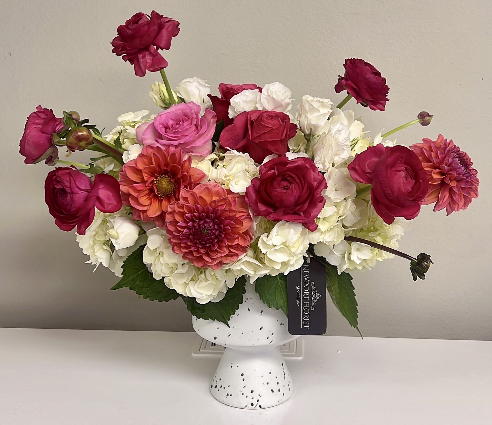 Rosy & Sweet NF-Y31 Rosy & Sweet NF-Y31 - Roses are such a special Symbol of love an Romance, and this beautiful and sweet design brings it all. White hydrangeas as the base and pretty colombian hot pink roses and coral-pink dahlias gives such an amazing touch to this beauty arranged in a white ceramic pedestal vase. Surprise your love one !