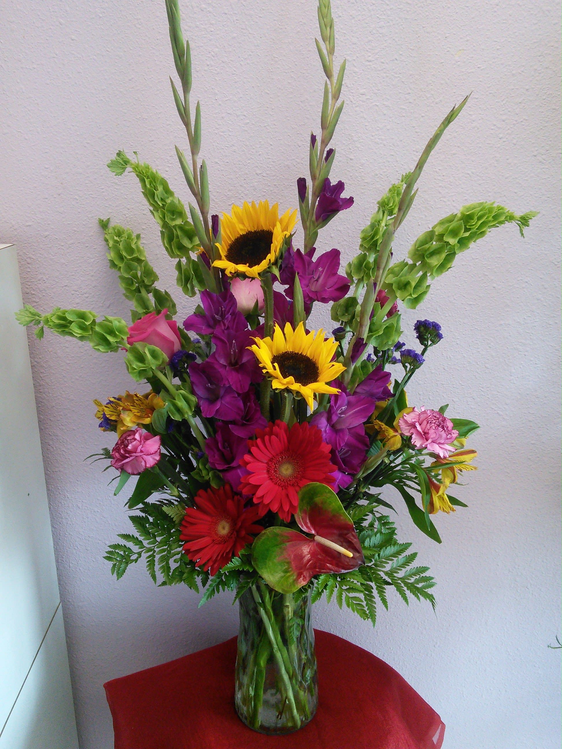 In The Dawn By Forever Flowers In The Dawn By Forever Flowers - Deep purple gladiolas, red gerberas, sunflowers and a more making this arrangement very unique and elegant with rich deep colors perfect for any occasion.