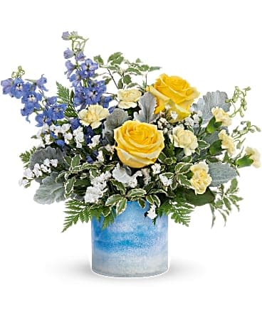 Teleflora's Seaside Dreams Bouquet - Like a stroll by the sea, this radiant yellow rose bouquet in an ocean-inspired art glass vase delights the senses. This dreamy bouquet includes light yellow roses, miniature light yellow carnations, blue delphinium, white sinuata statice, dusty miller, pitta negra and leatherleaf fern. Delivered in a Color Frost Art Glass cylinder.