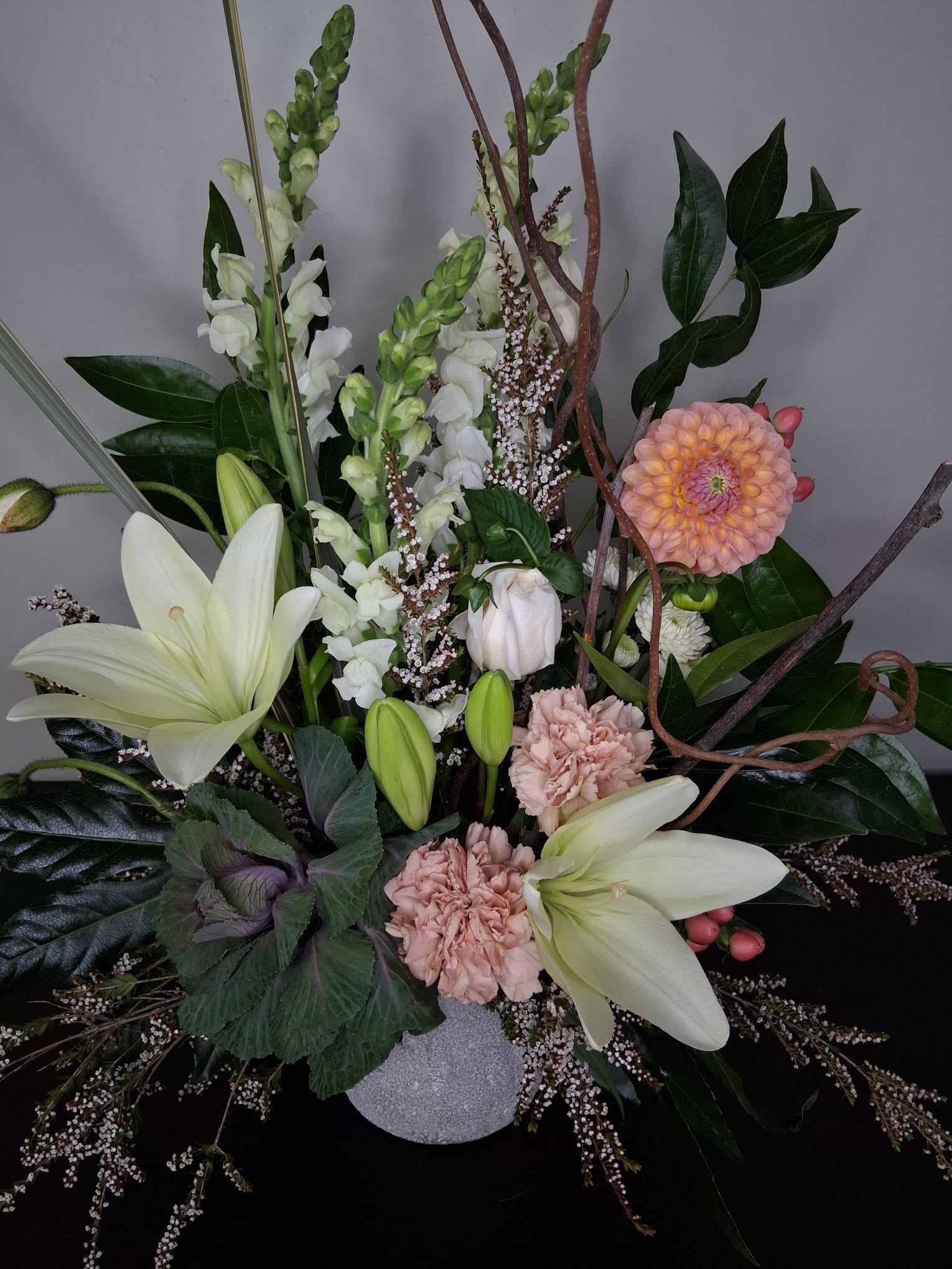 Graceful Meadows  -  Spilling out and over with grace, these playful dahlias and snapdragons standout  amongst the lush greenery and stone container. Soft tones with a pop of color lend this arrangement a gentle feel that's great for all occasions. 