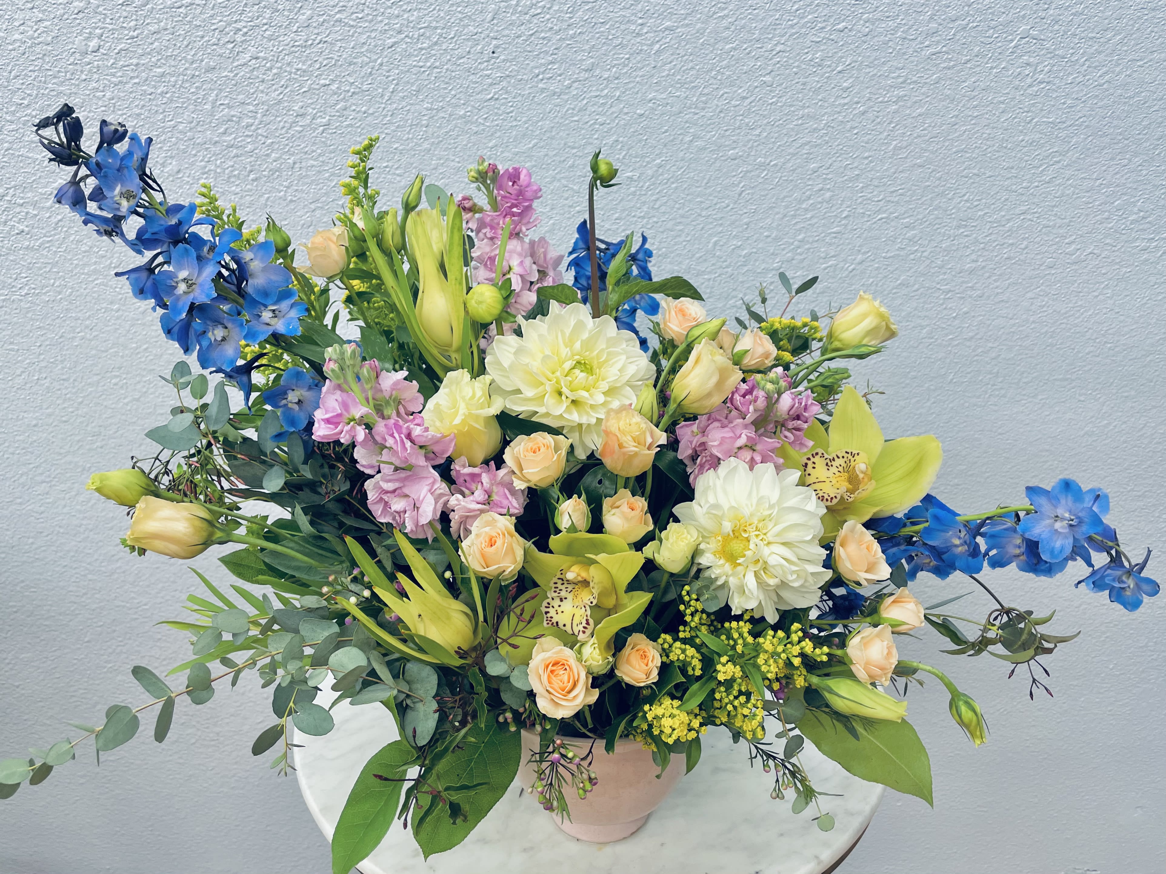 Seasonal Designers Choice  - Color Palette: Mixed Let our designers choose the freshest and most beautiful flowers to design a custom arrangement for you. Tucked into botanical eucalyptus and seasonal greens in a simple ceramic container.  *Photo shows deluxe upgrade*