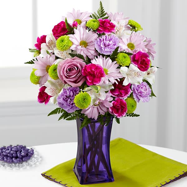 The FTD Purple Pop Bouquet - The FTD&reg; Purple Pop&trade; Bouquet comes straight from our fun trendy and simply irresistible Color Confection Collection. Perfectly grape this stunning flower bouquet consists of lavender roses carnations and traditional daisies offset by fuchsia mini carnations green button poms and white Peruvian lilies to create an arrangement popping with color and style. Presented in a violet purple glass vase to give it a poshly purple pop look this mixed flower arrangement is set to send your sweetest wishes to friends and family in honor of a birthday as a thank you or just to celebrate in style.