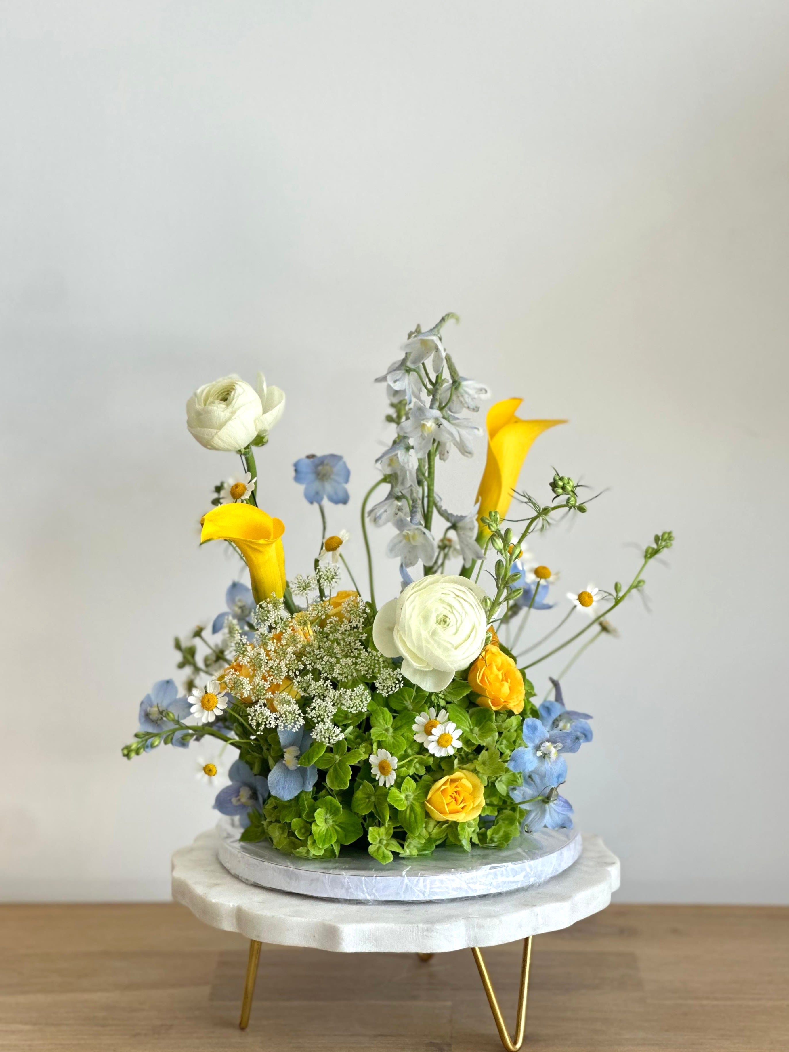 Yellow Flower Cake Box  - A flower arrangement in the shape of a cake, with yellow, green, and blue flowers. Comes in a gift box.   Flower types may vary depending on the season.