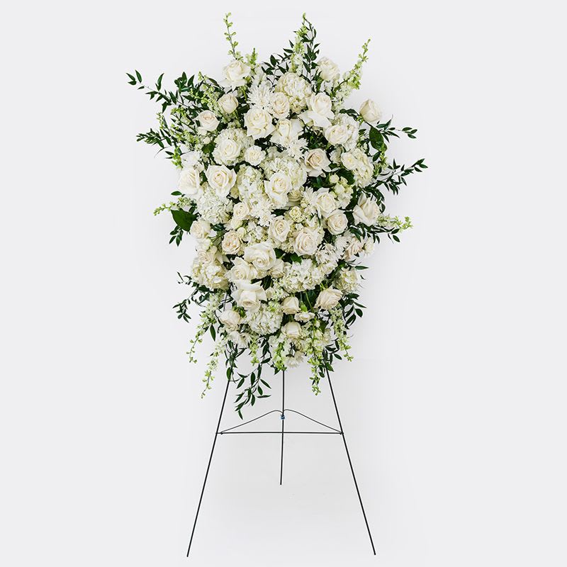 Funeral Standing Spray - A timeless design featuring a mix of premium and seasonal white blooms accented by textural greenery.  Placed upon a 5’ wood easel, included.