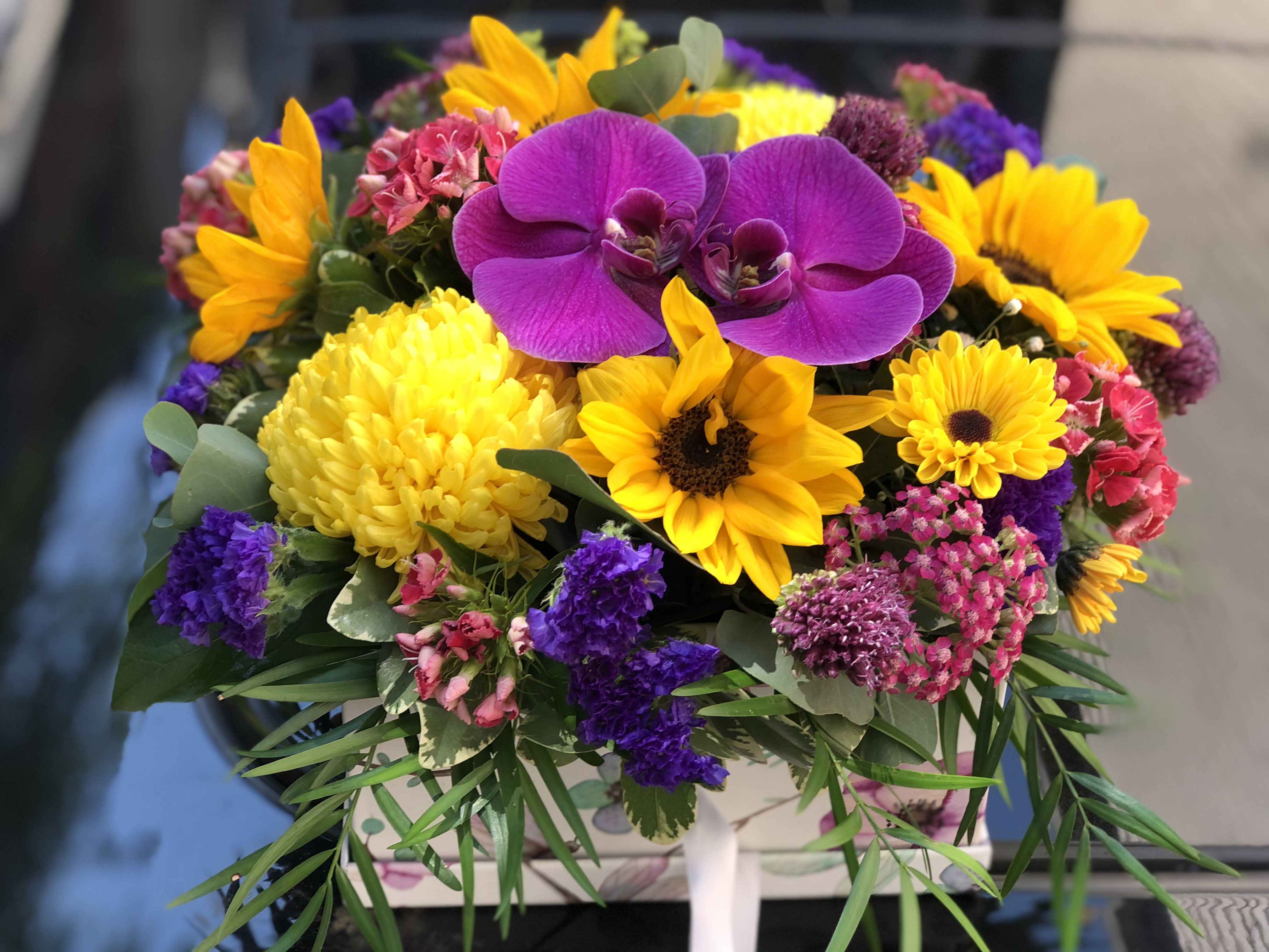 Sun-Kissed: summer flowers in a box Sun-Kissed: summer flowers in a box - A beautiful and cheery collection of locally grown summer flowers kissed by colorful orchids and arranged in a fun box that can later be re-used.
