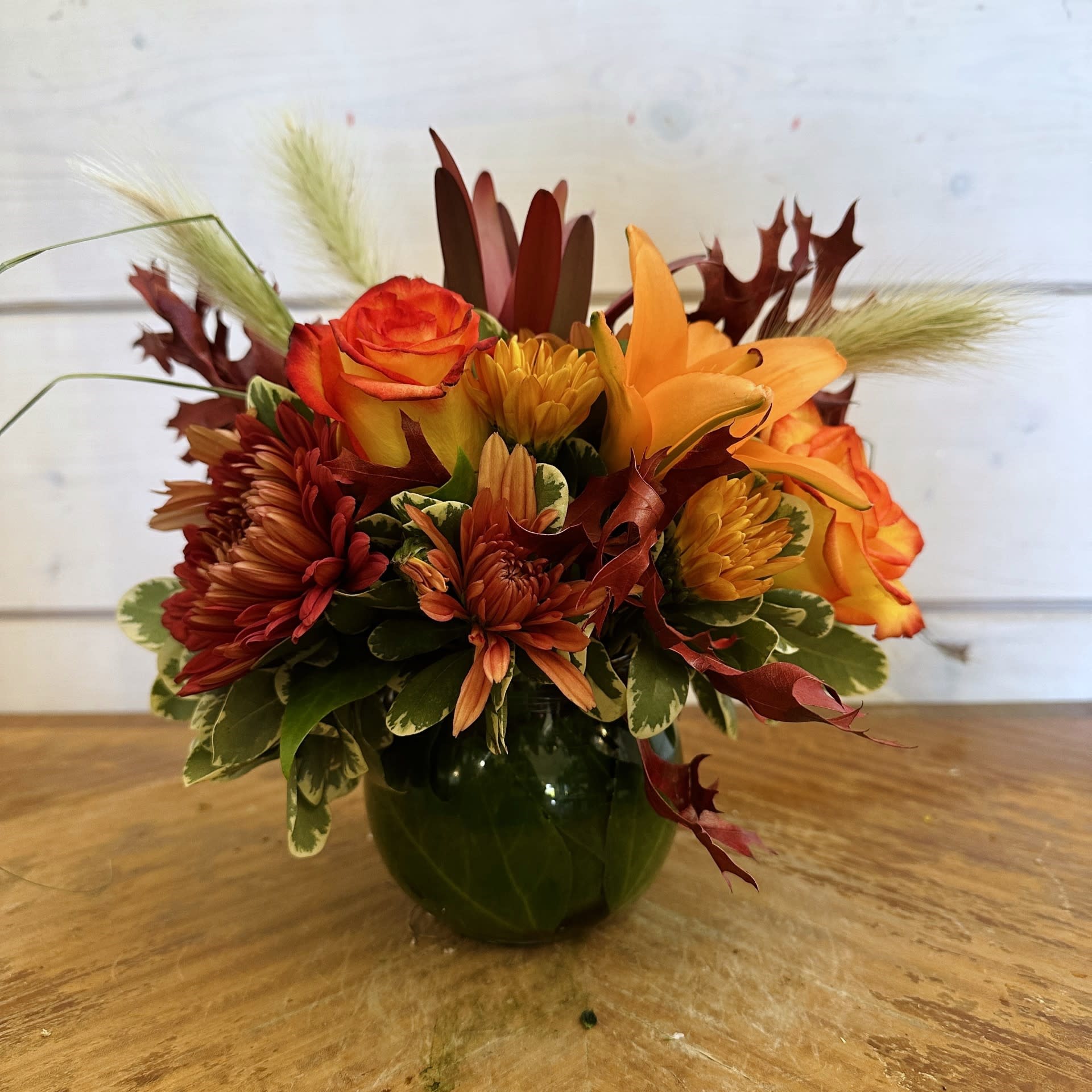 Amber Sunrise Bouquet Amber Sunrise Bouquet - Orange roses, orange lily, safari sunset, fall chrysanthemums, and fresh bunny tails arranged in a 3in leaf lined bubble bowl with burgundy oak leaves. Approximately 8in tall and 8in wide.