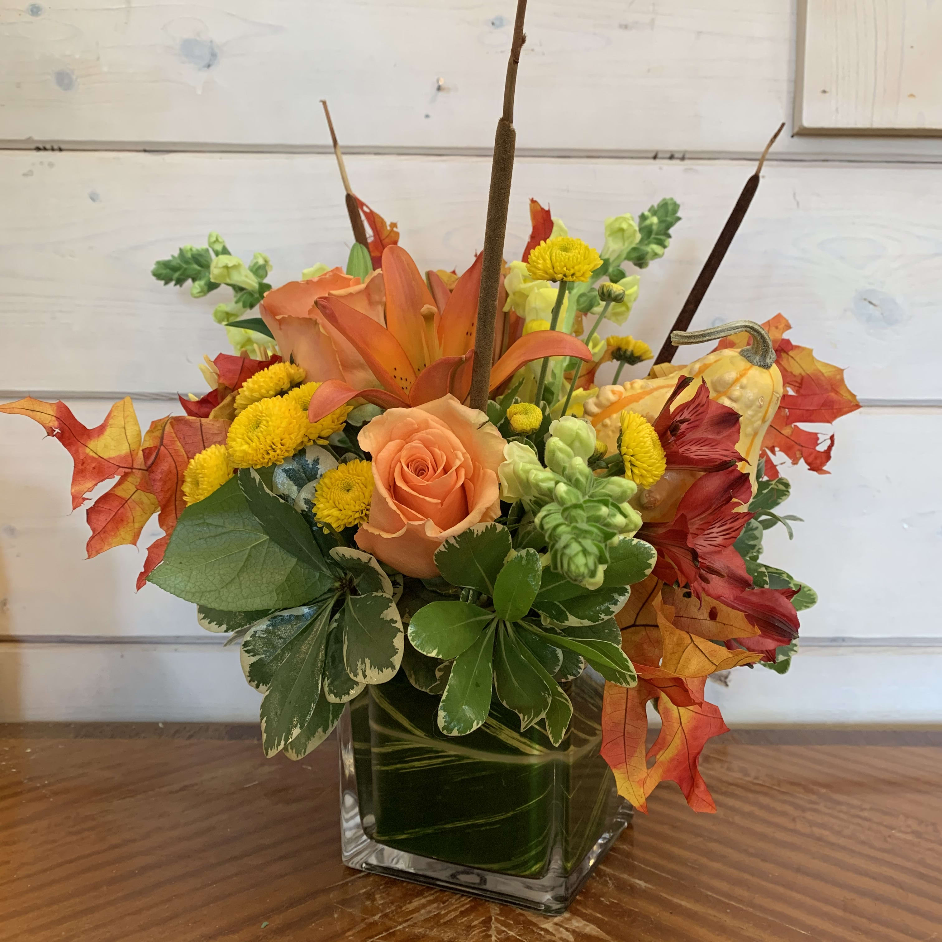 Autumn Rainbow Autumn Rainbow - Apricot roses, fall lily, yellow snapdragons, red alstromeria and yellow buttons arranged in a leaflined cube with bright fall foliage, cattails, and a gourd insert. Approximately 12in tall and 10in wide.